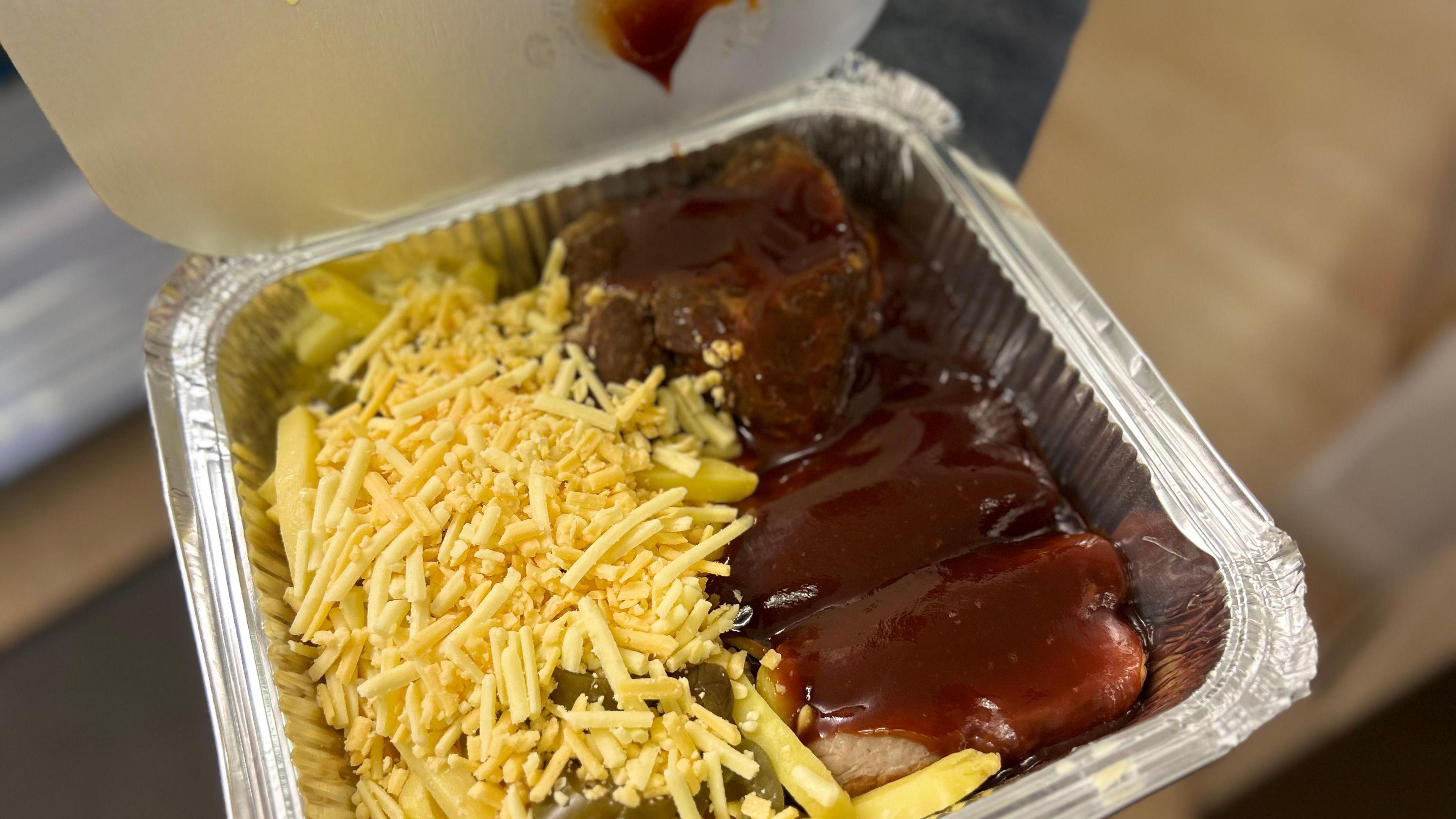 Loaded fries with pork and barbecue sauce in a metallic tray.