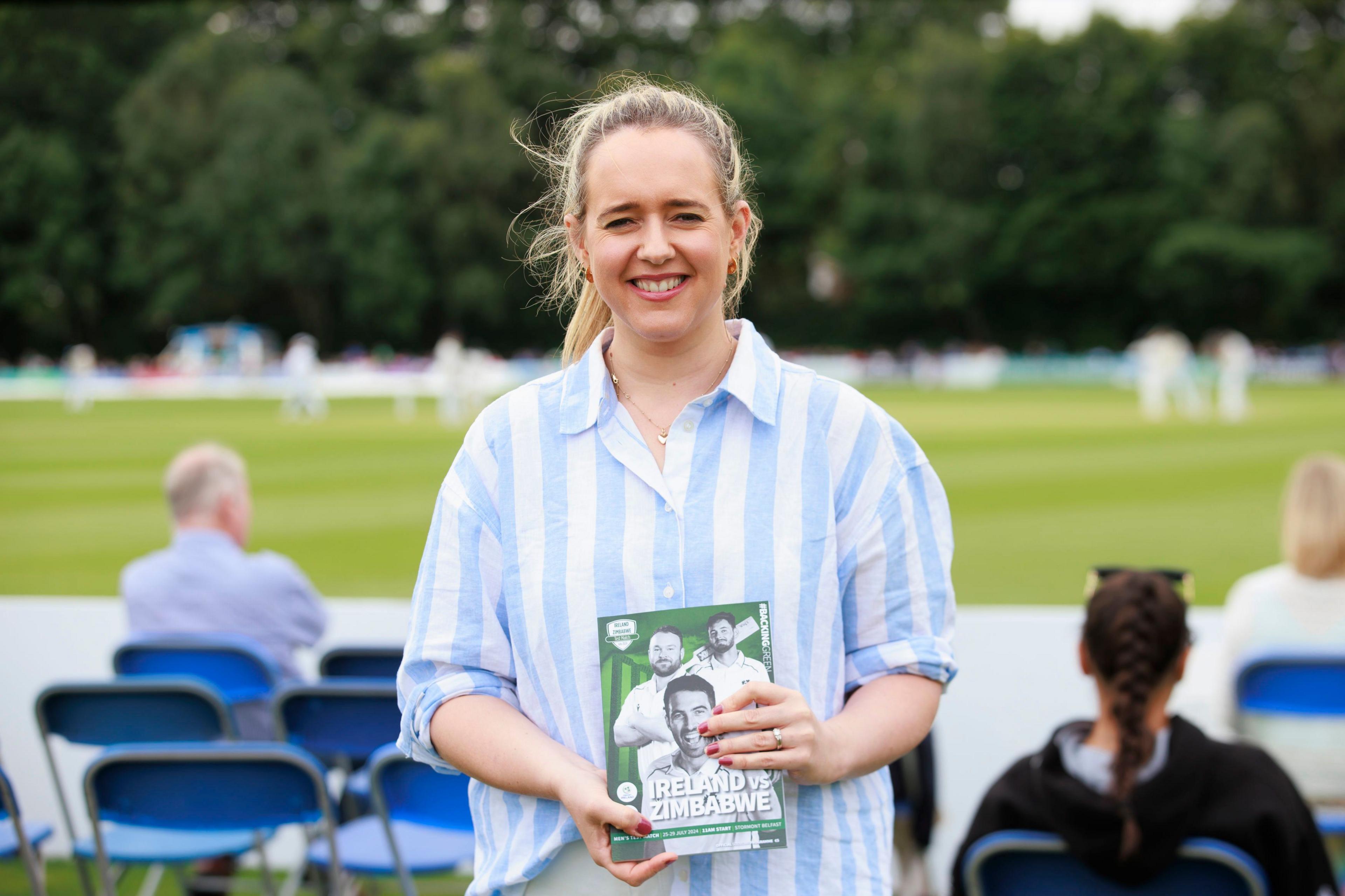 Kate Nicholl standing at the test match holding a Ireland Zimbabwe flyer 