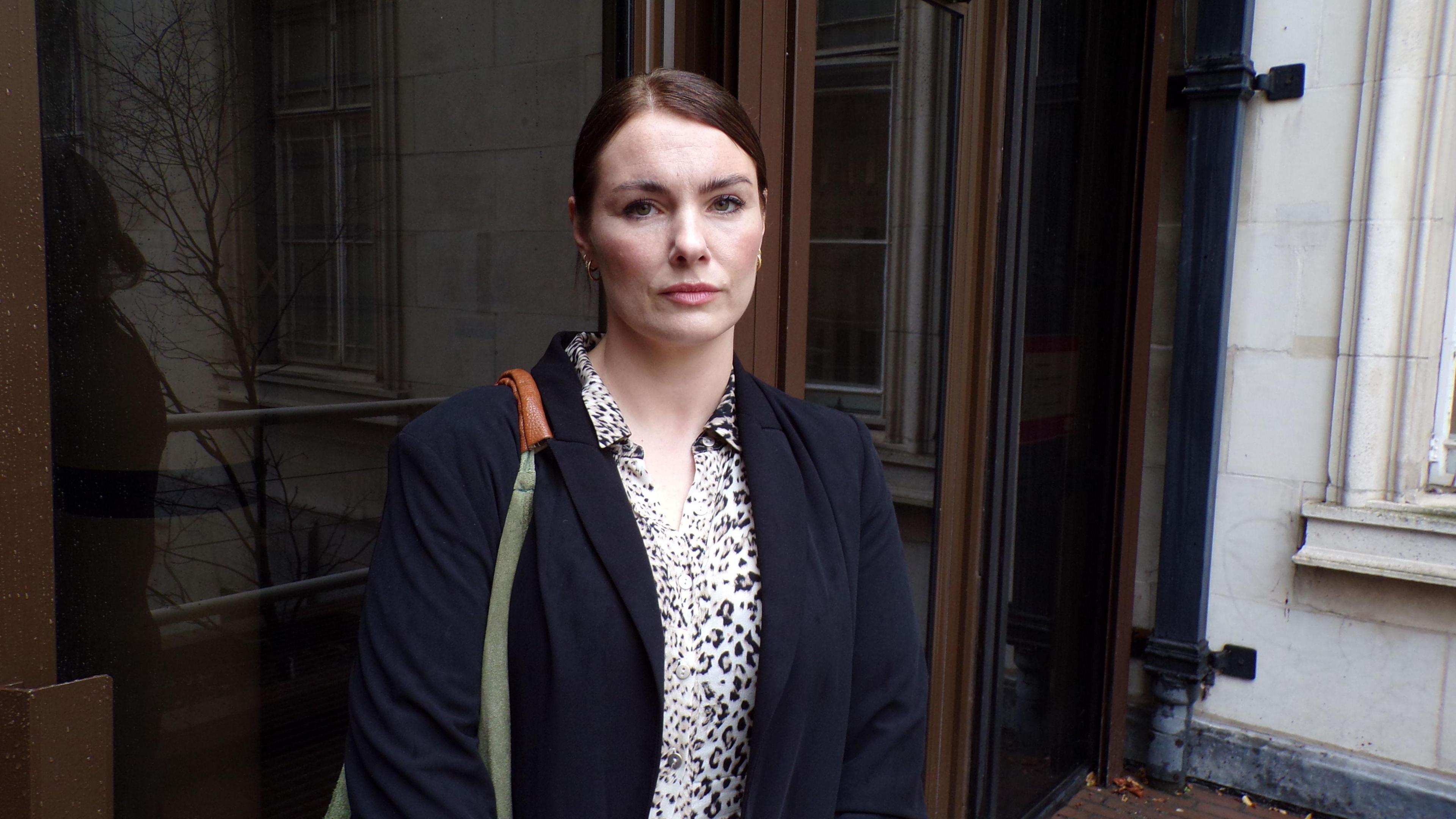 Hannah Harding in a navy blazer standing outside the wooden doors of County Hall