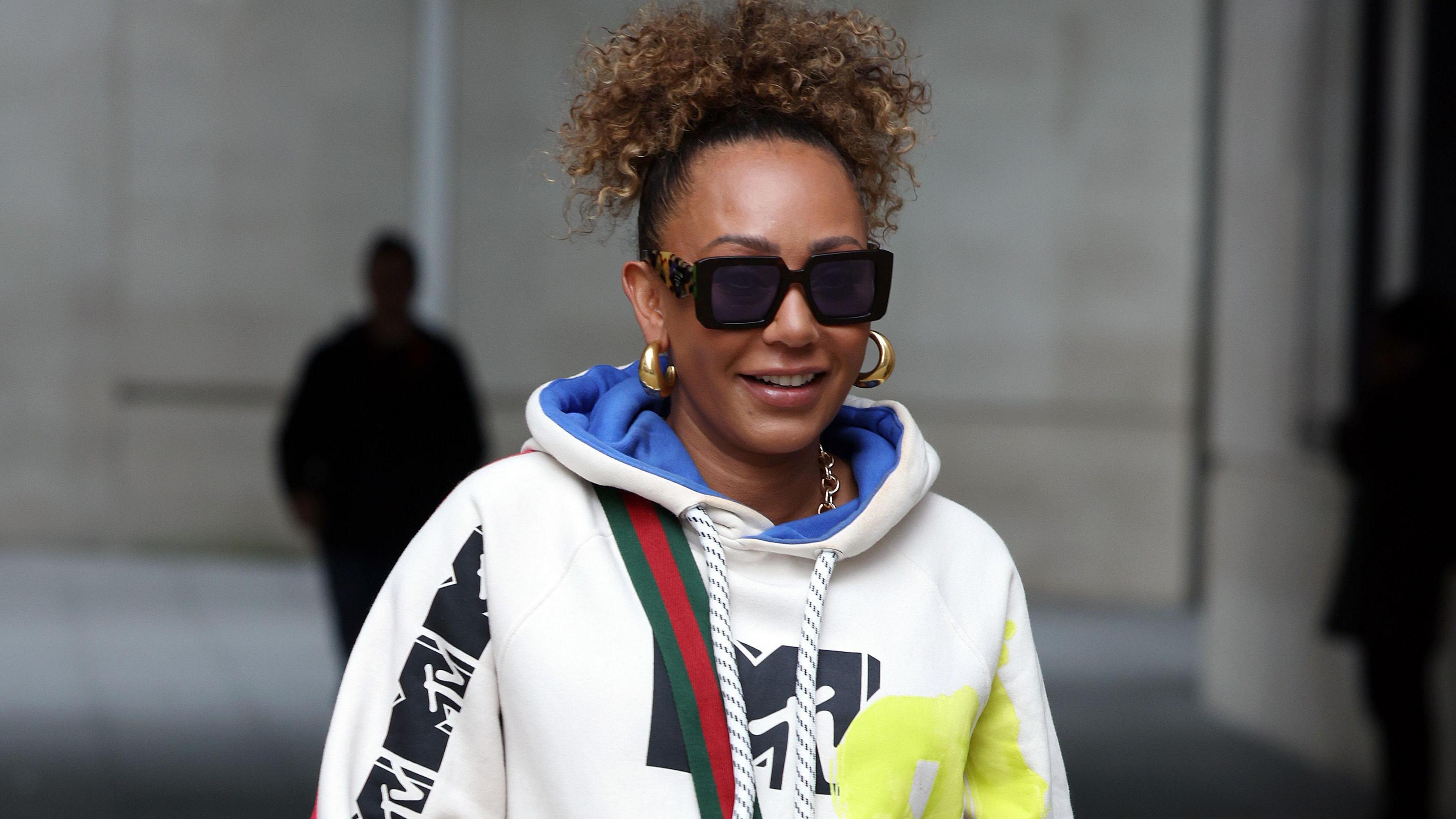 Mel B walking down a street wearing sunglasses and an MTV-branded hoodie.