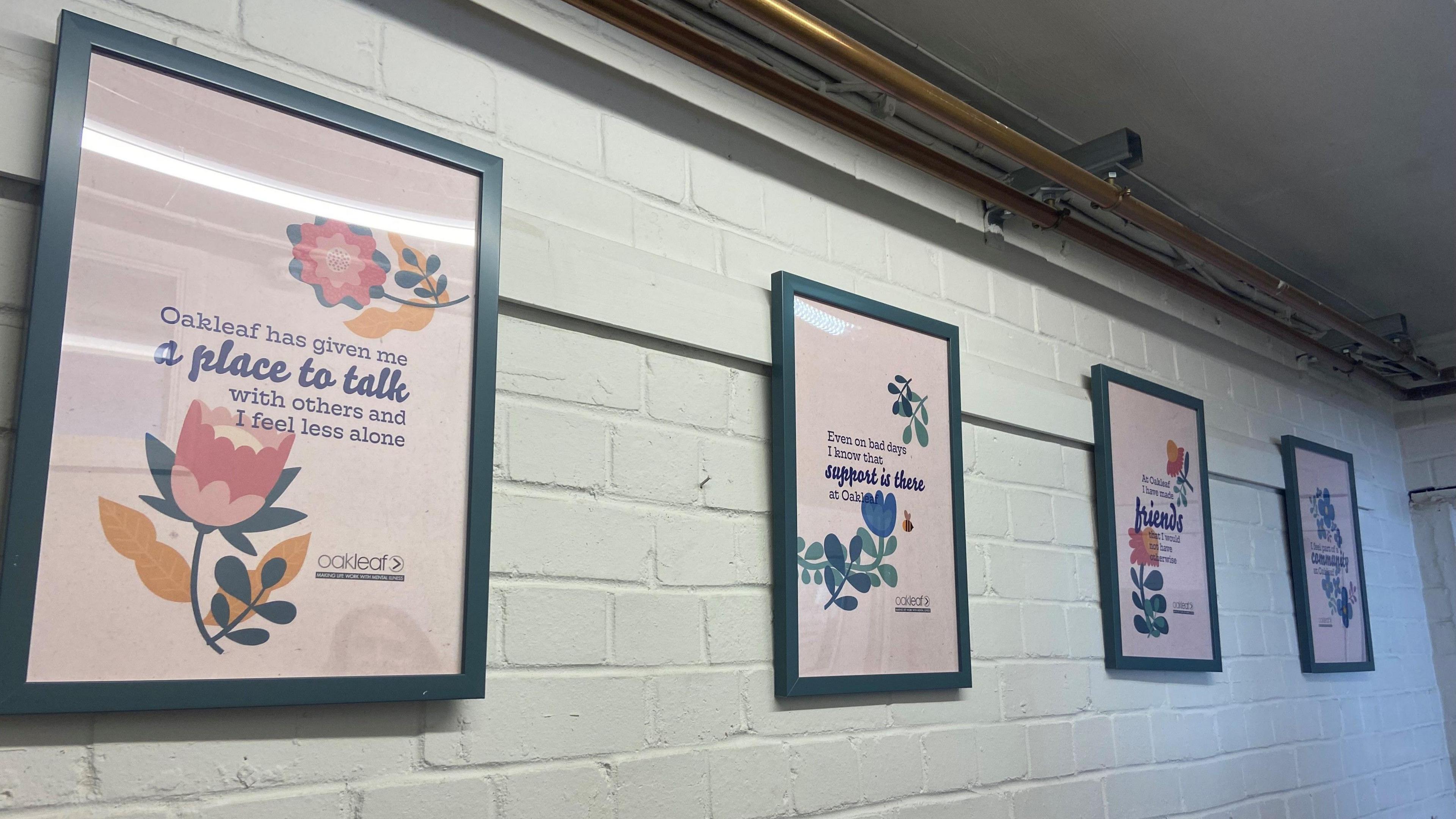 Framed posters on a wall, the first of which reads: "Oakleaf has given me a place to talk with others and I feel less alone"