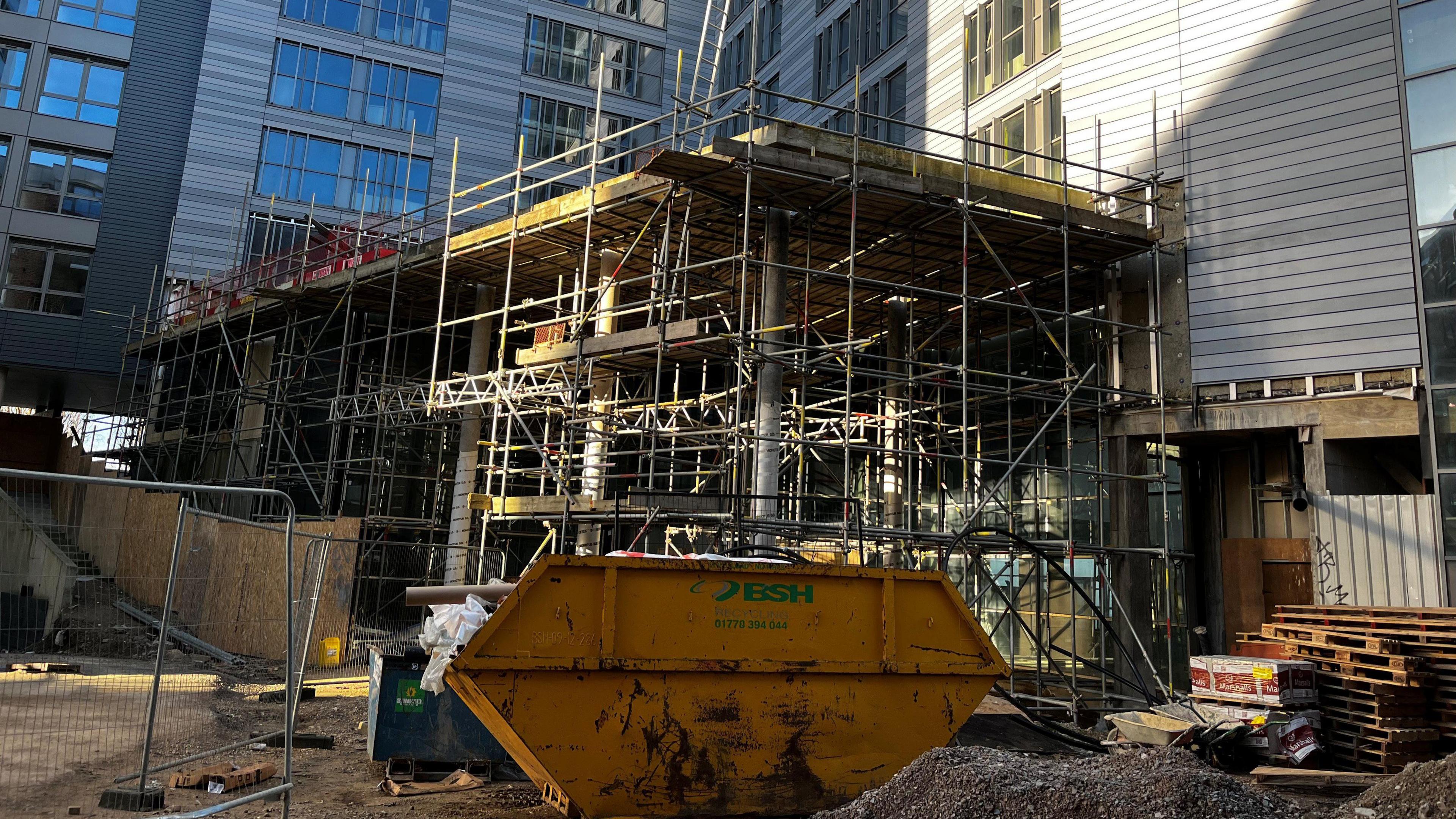 A yellow skip and scaffolding outside the hotel.