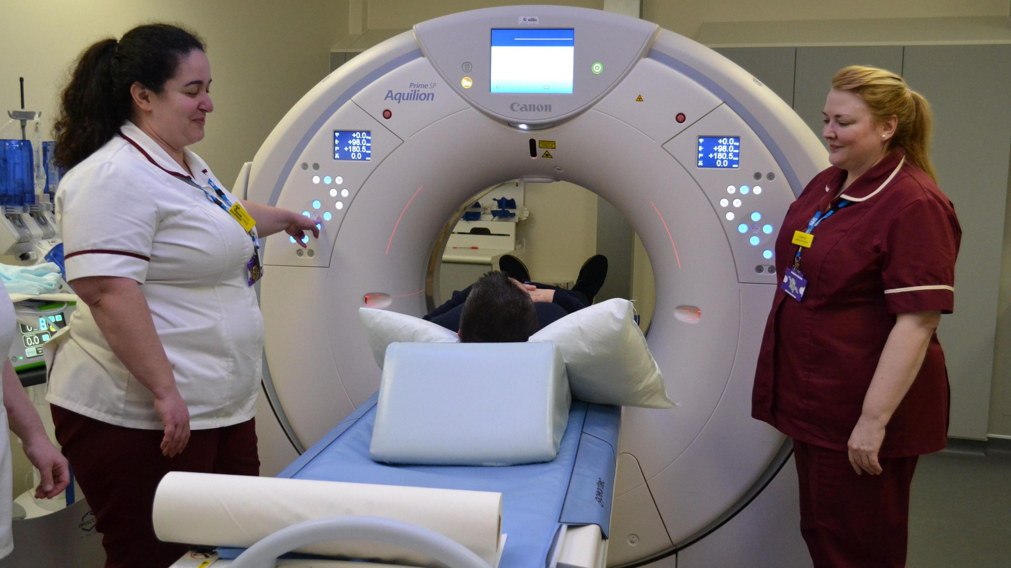 A person going into a large CT scanner with two nurses standing nearby