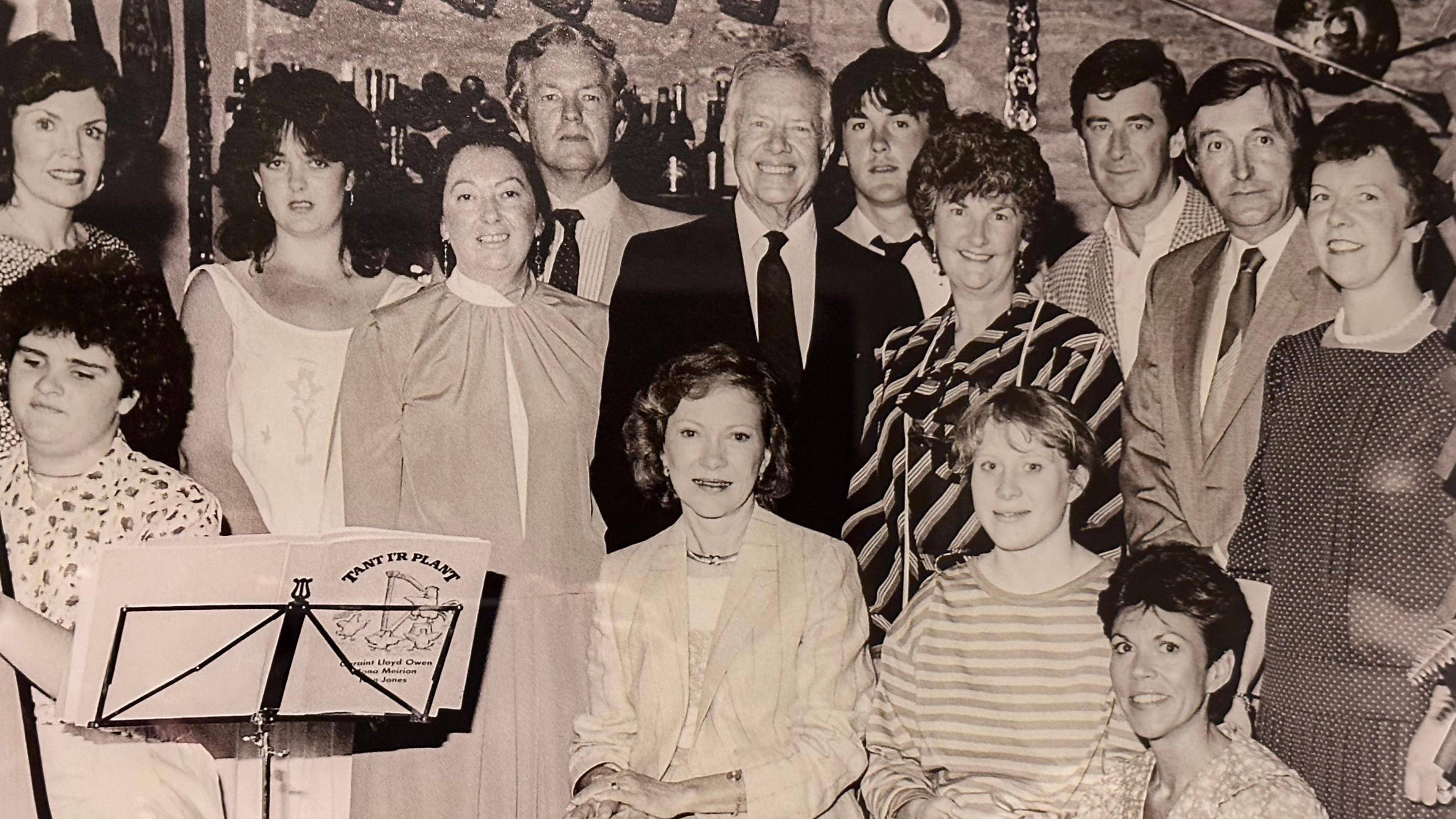 A black and white photo of the group of musicians which performed form Jimmy Carter in Y Talbot Hotel, Tregaron. Included in this photo are Mr and Mrs Carter, their daughter Amy, Eirioes Ayres and the harpist Rhian Davies