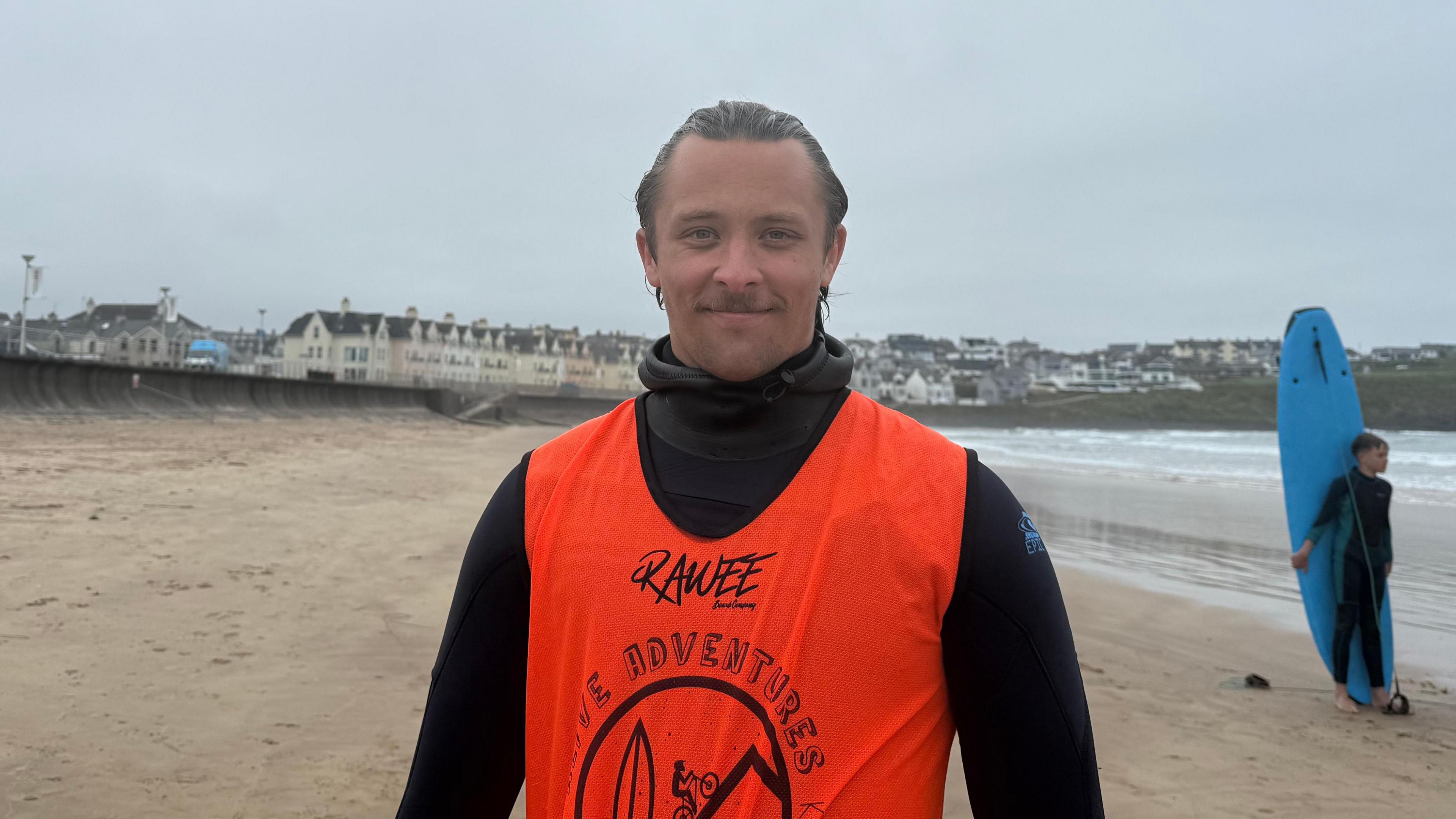Andrzej Krystowski. He has brown hair, wearing a black wetsuit with orange vest.