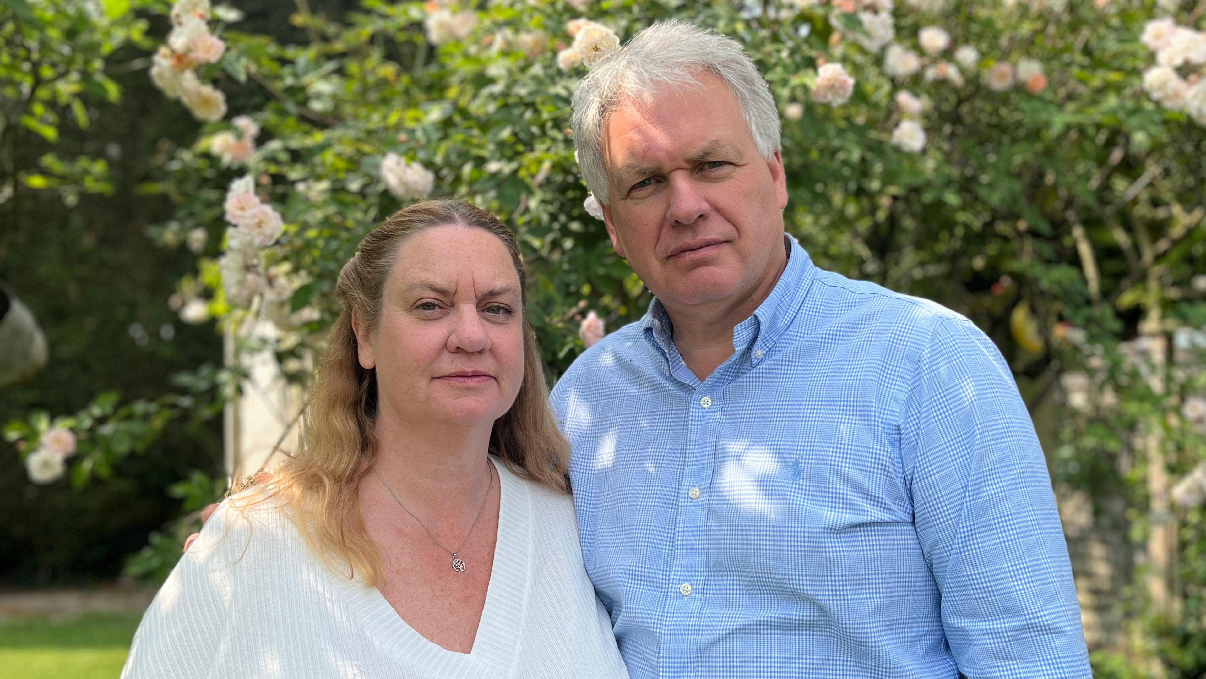 Anthony Newborough wearing a light blue shirt with his arm round Elaine Newborough who is wearing a white top. They are in a garden.