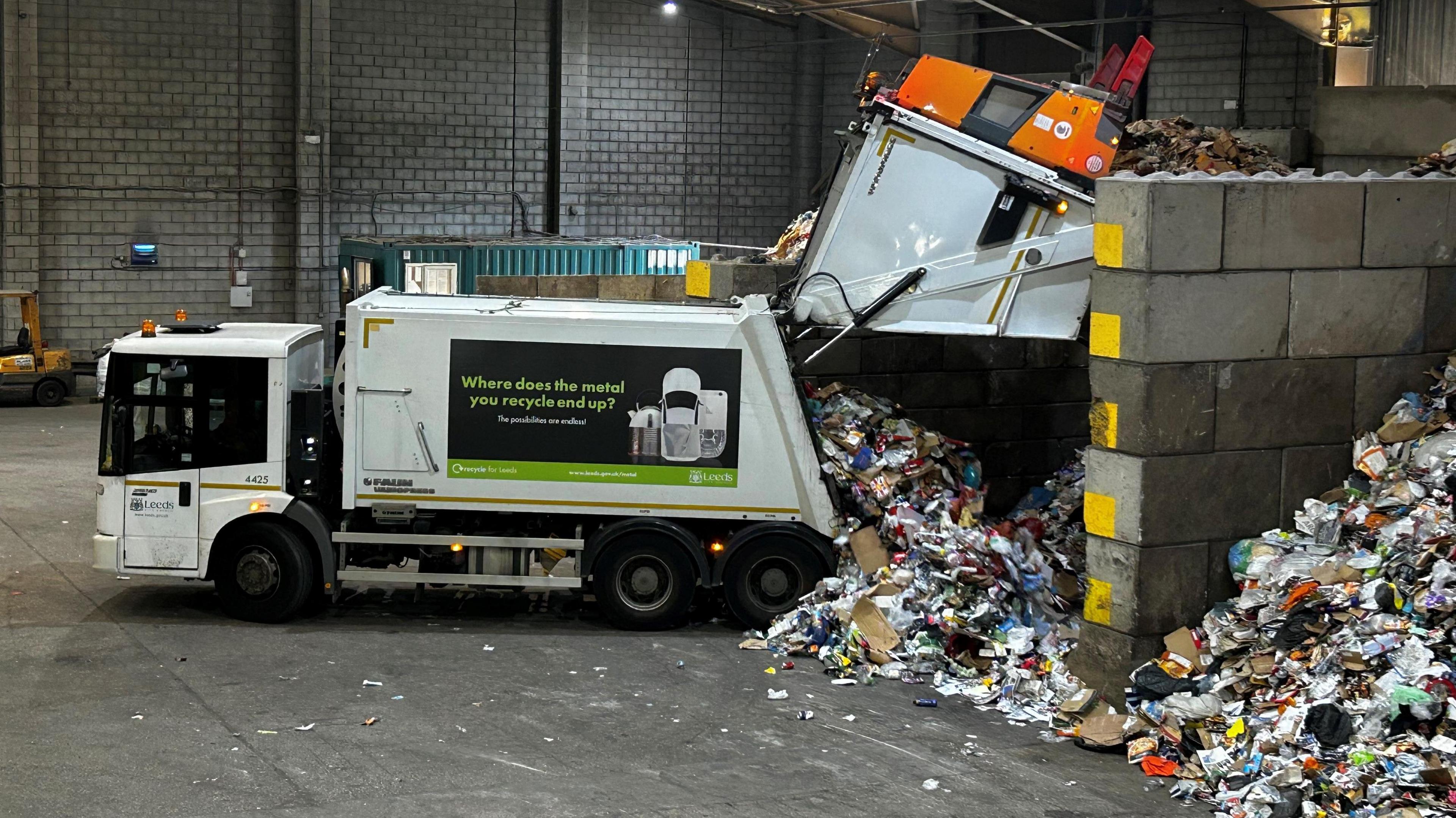 A Leeds recycling lorry unloads material on to a pile of recyclable materials inside a warehouse