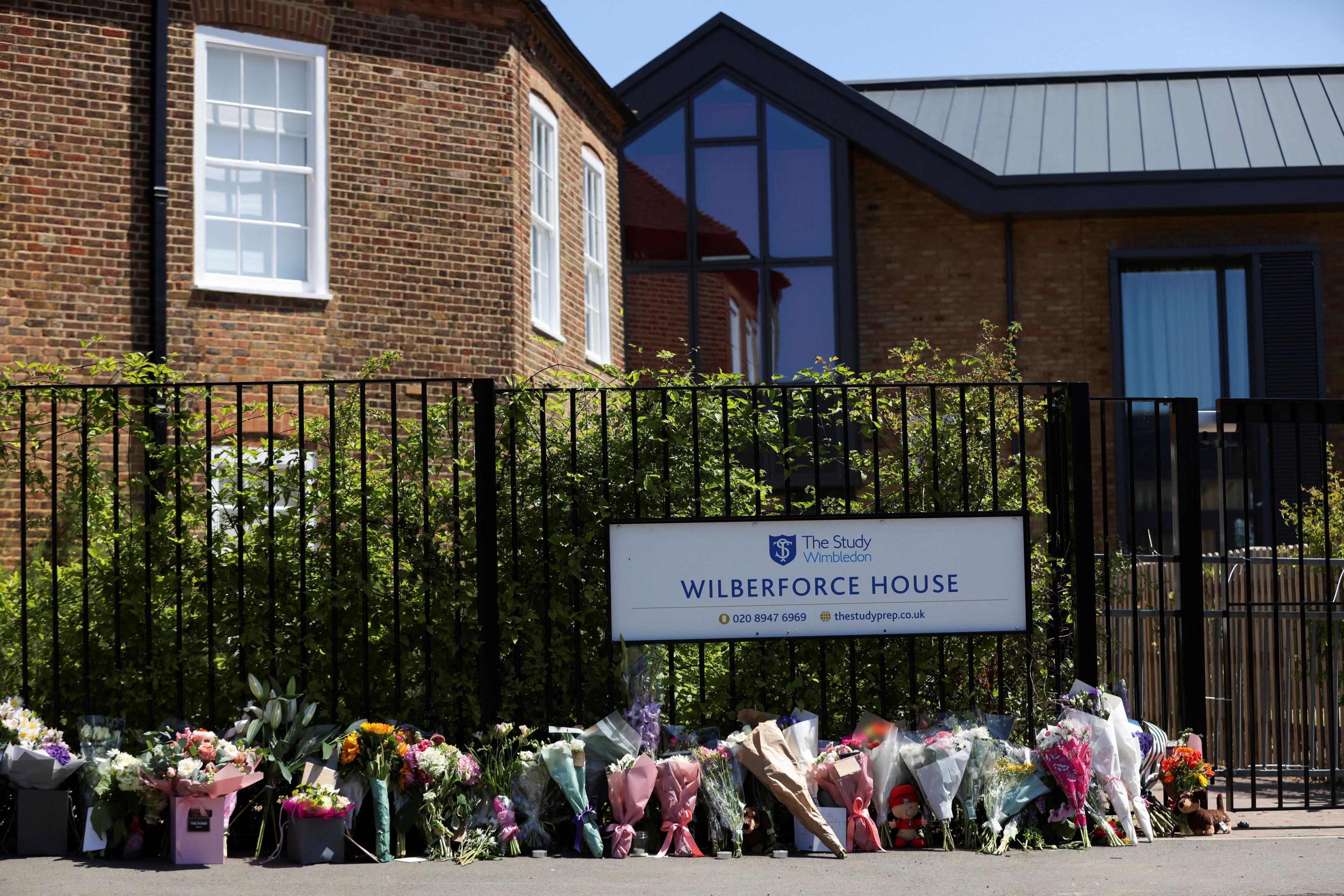 Floral tributes are laid outside a school gate under a sign for Wilberforce House