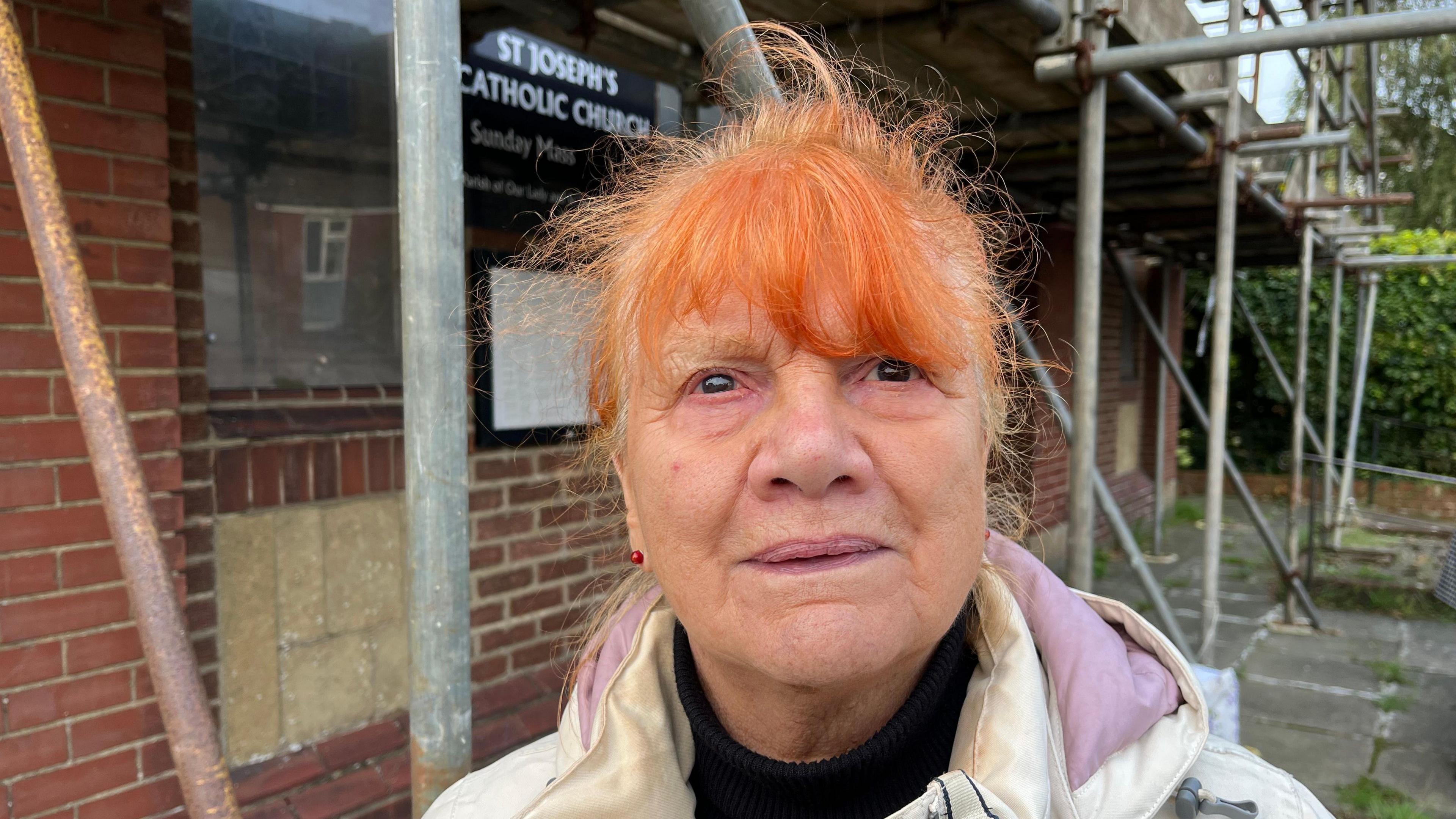 Margaret Irving looks at the camera, behind her you can see the scaffolding on the outside of the building and the sign on the front of the church