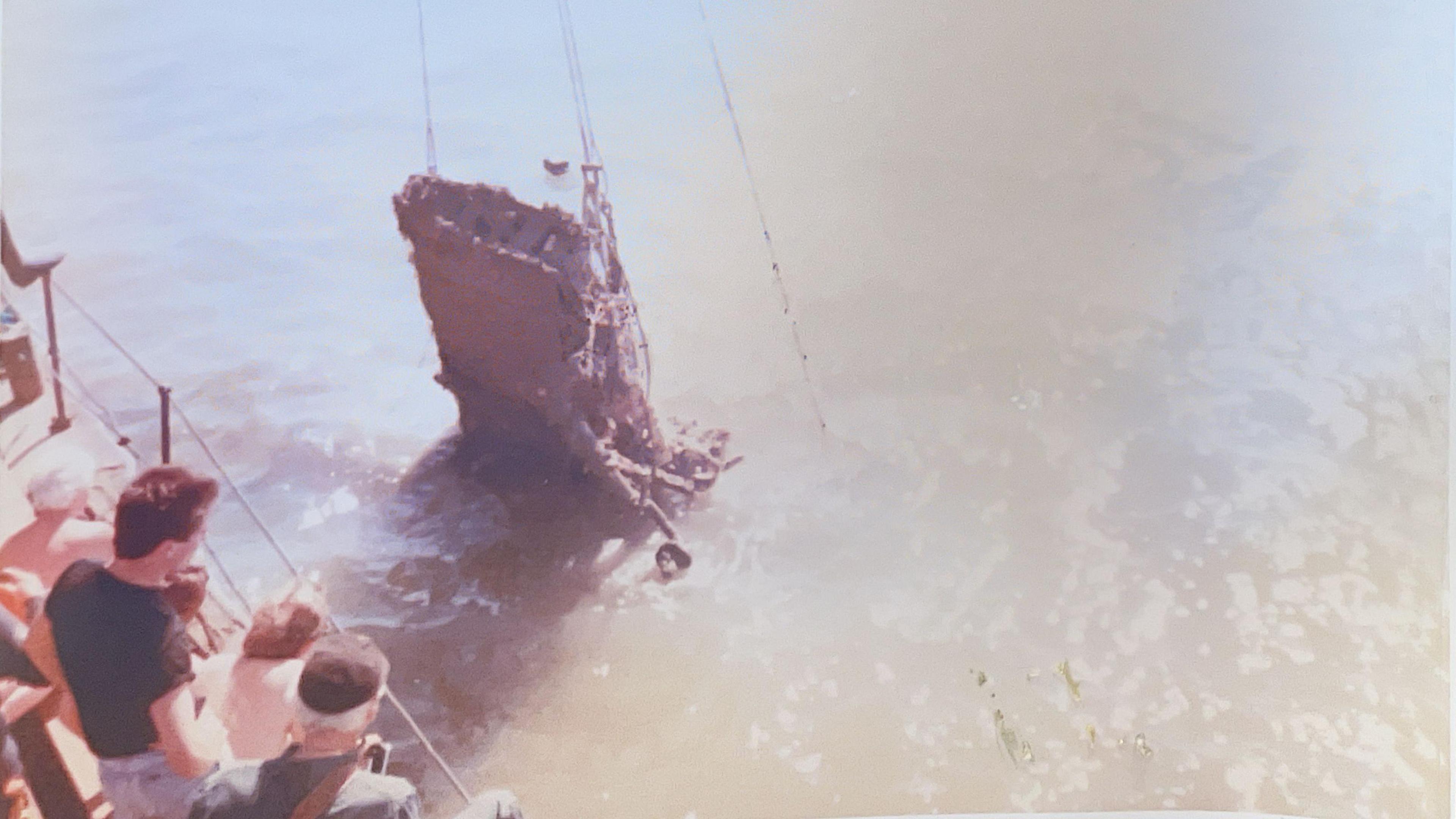 An old photograph shows people gazing over the side of a wire fence on a boat as the wreck of an aircraft is pulled from the water by cables.