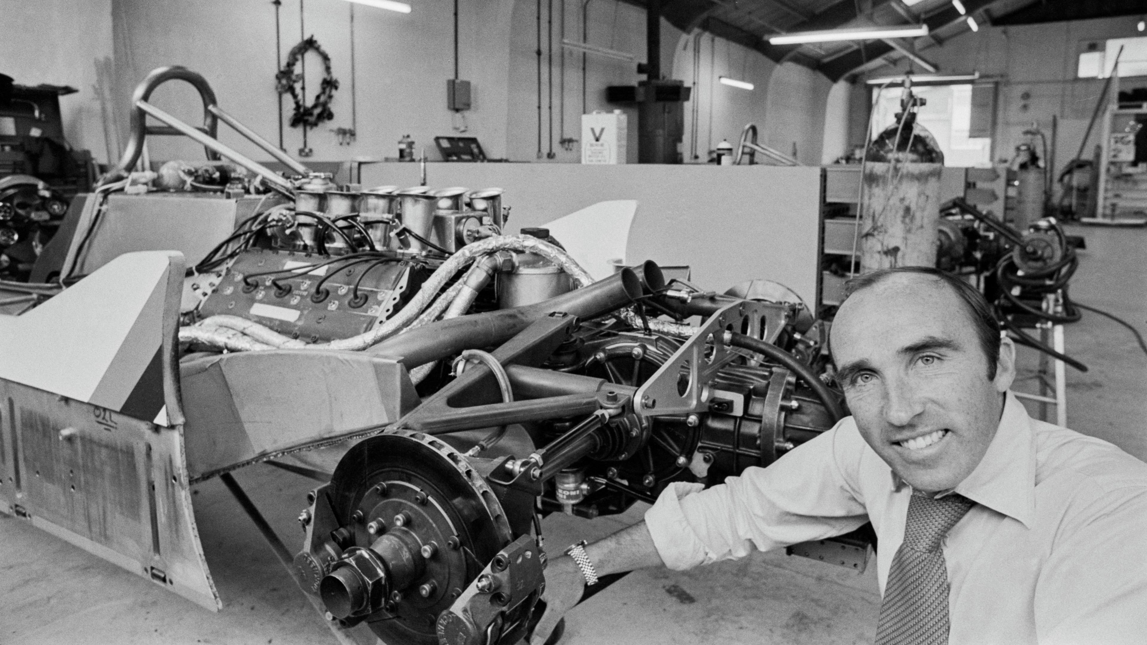 British businessman and motorsport executive Frank Williams, Williams Racing co-founder, poses with the Williams FWO7 (Ford Cosworth DFV V8 engine) in the Albilad-Saudia Racing Team workshop at the Williams Racing headquarters in Didcot around 1979.