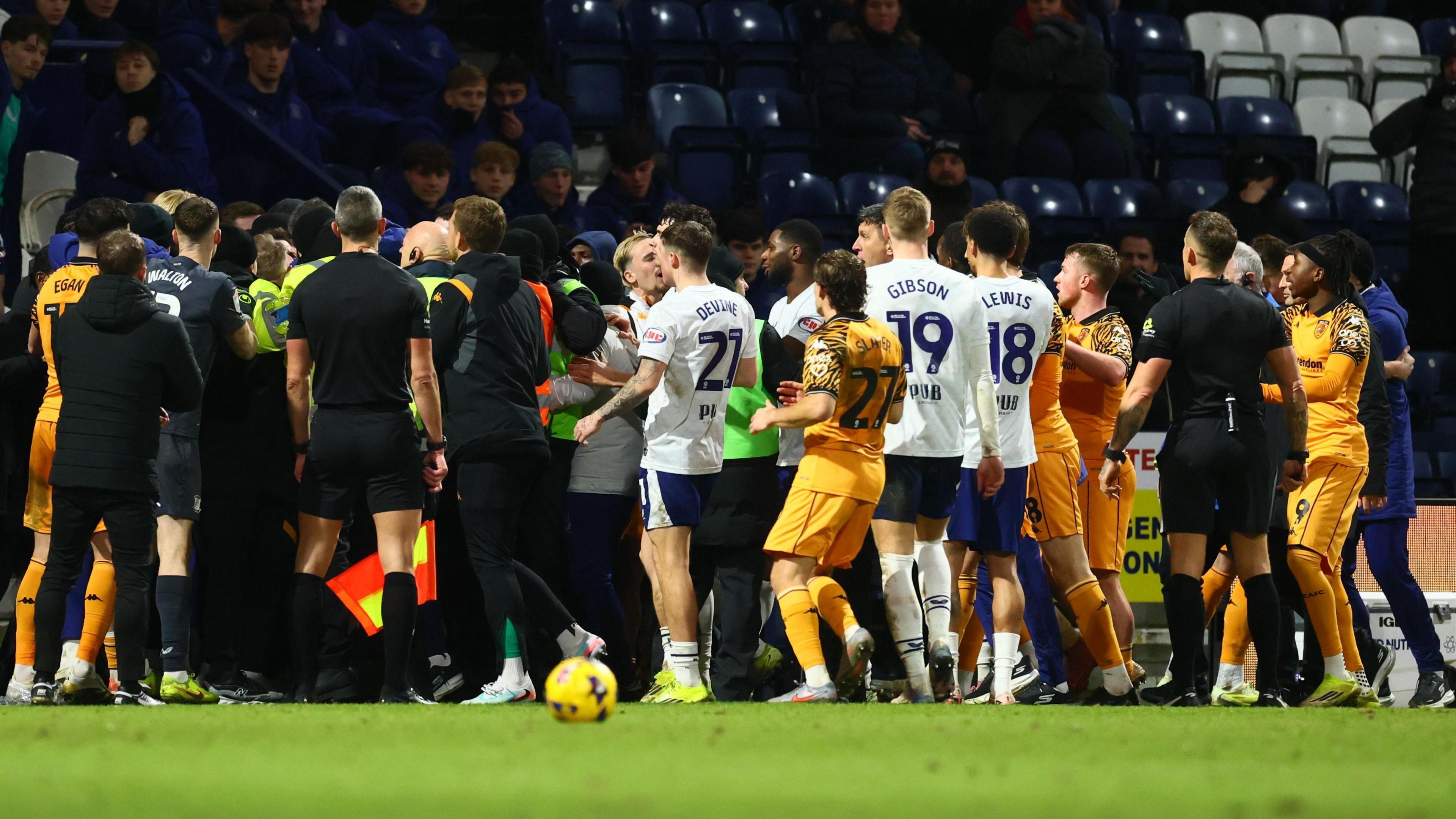 There is a coming together involving players of both Preston and Hull City with stewards in lime green bibs and some with fluorescent jackets trying to separate members of both sides' backroom teams 