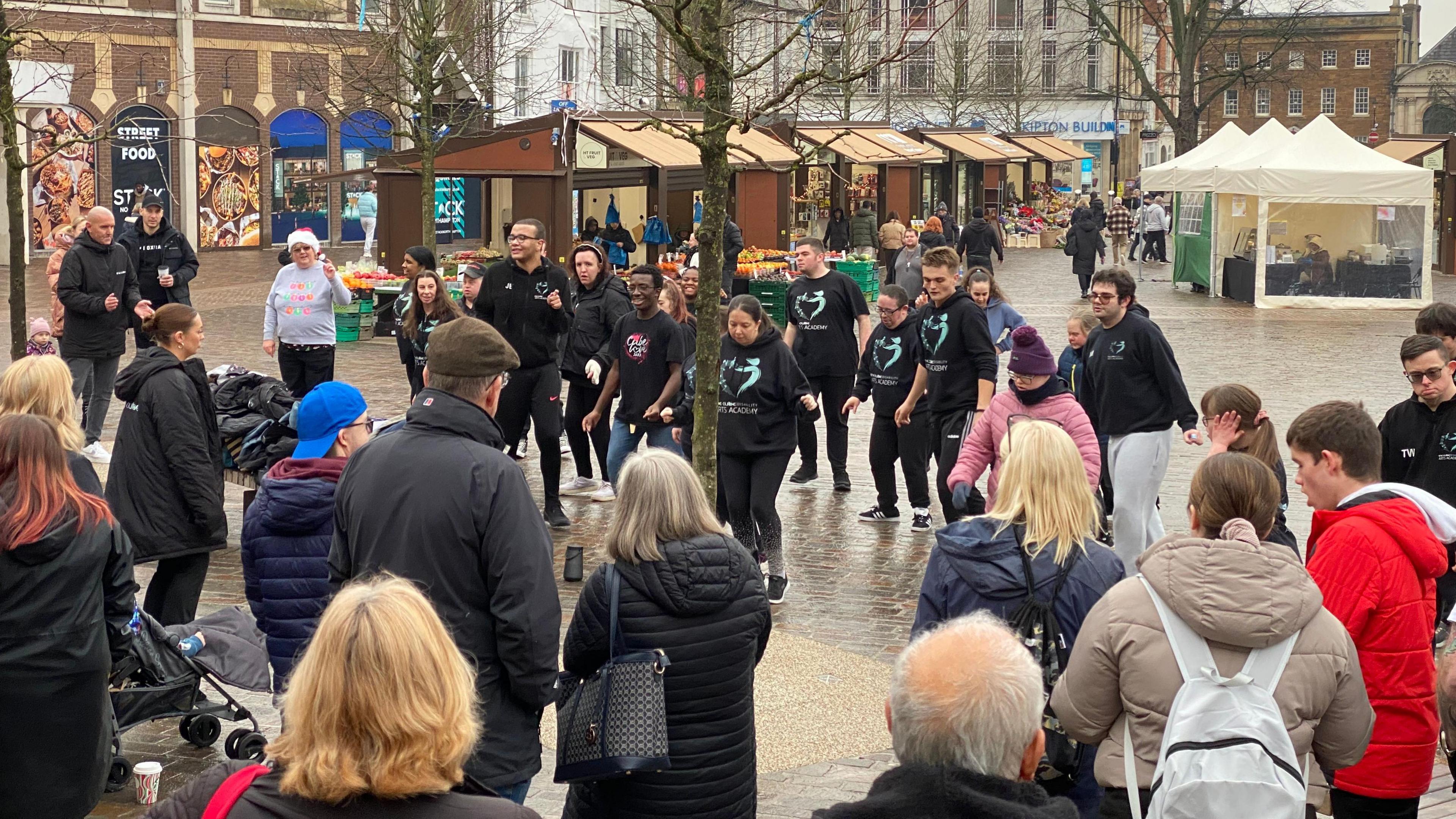 A group of people dressed in navy jumpers in the midst of a dance routine while a crowd of people watch.