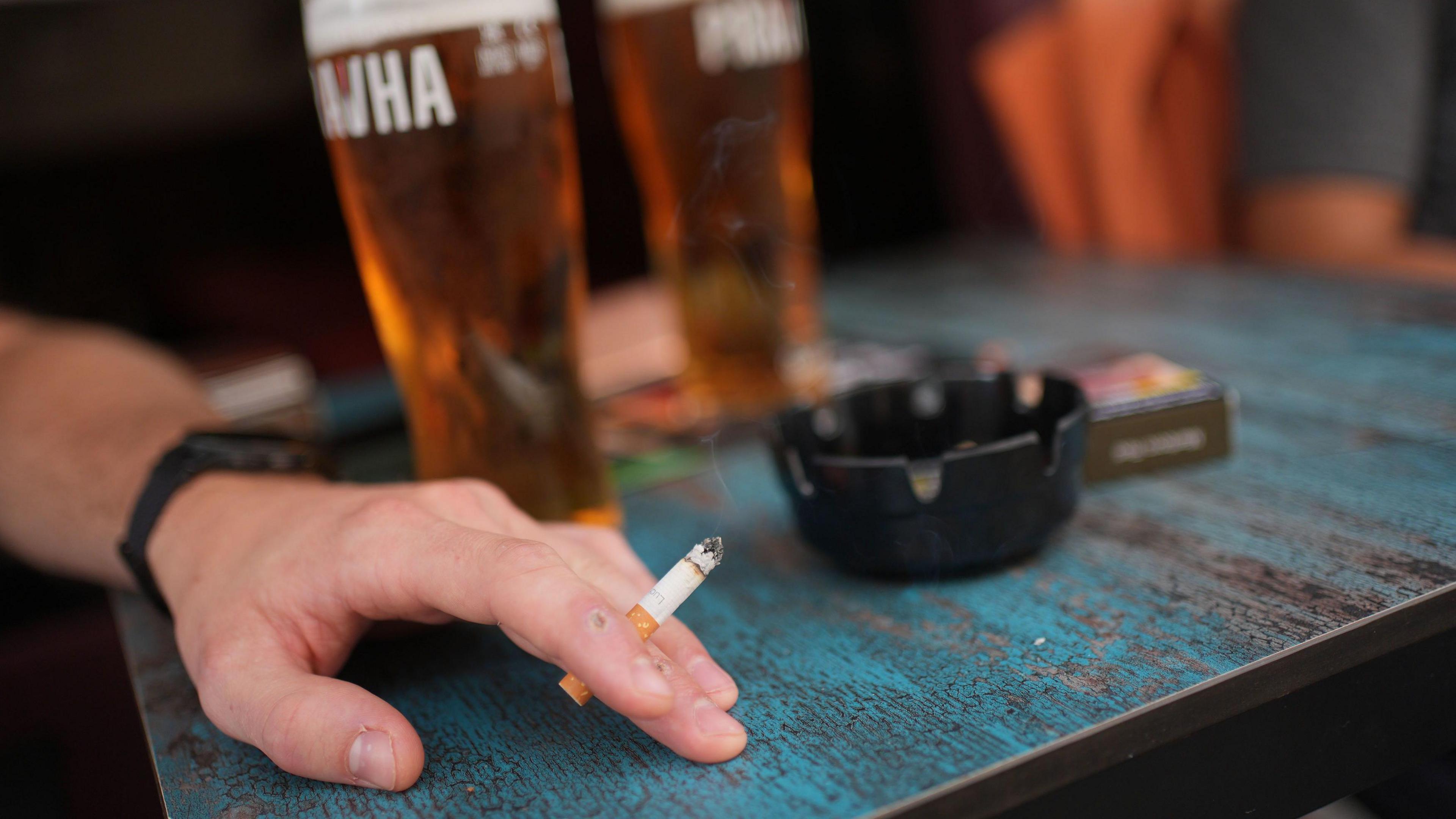 Stock picture of a man smoking a cigarette with a pint of lager outside a pub