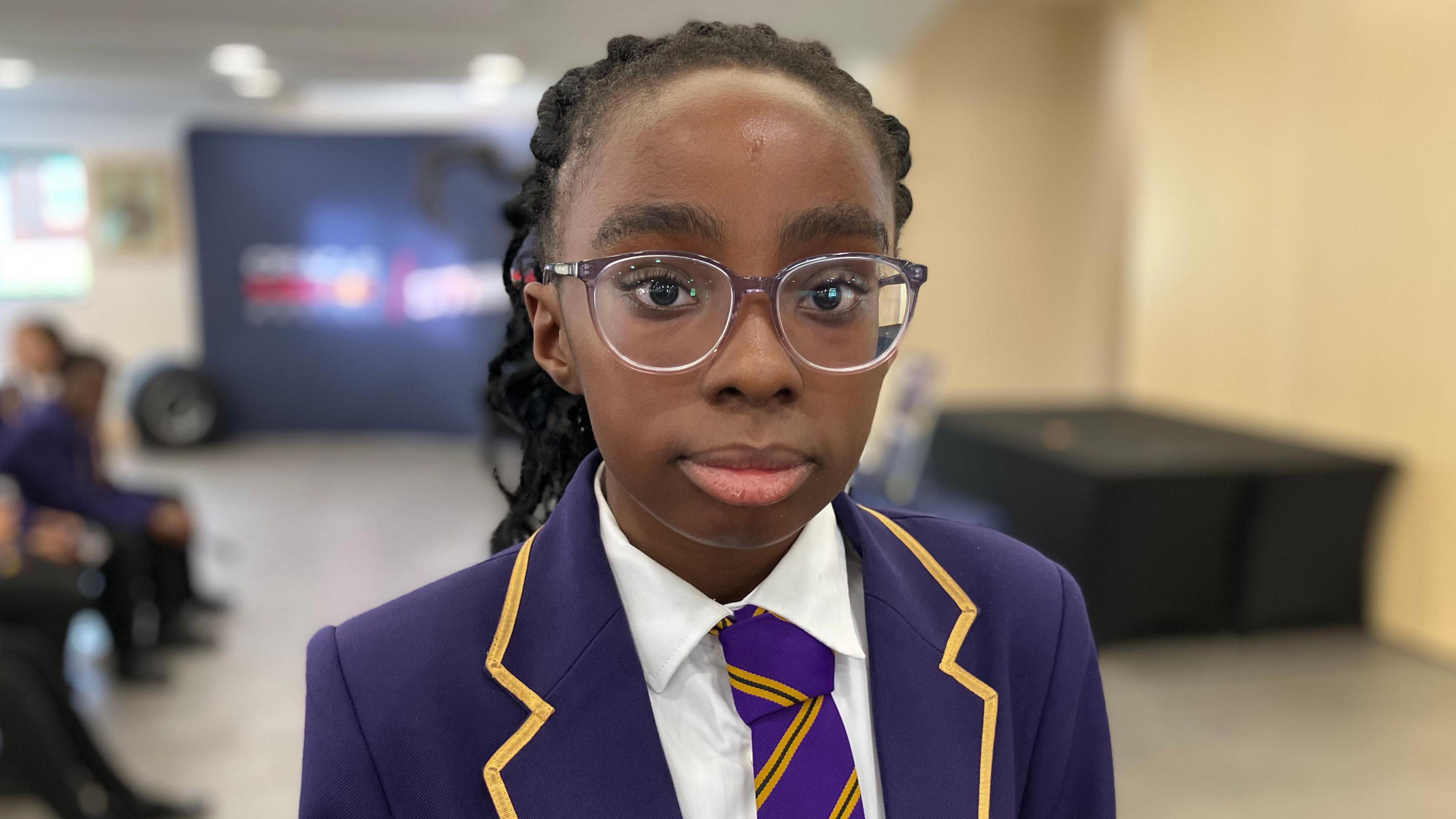 A young girl with glasses and wearing a purple school uniform.