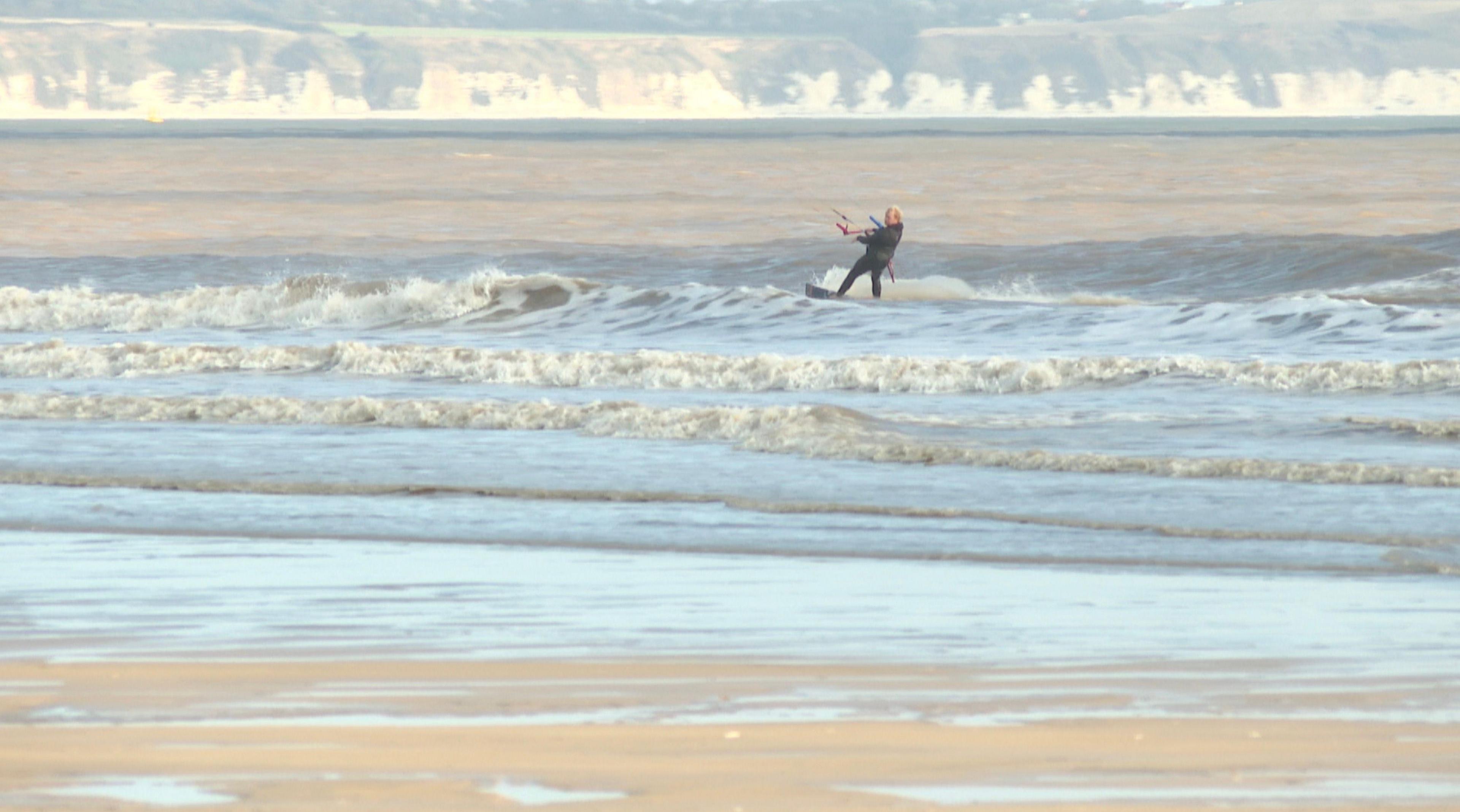 A windsurfer in the sea at Fraisthorpe beach. Cliffs can be seen in the background. 