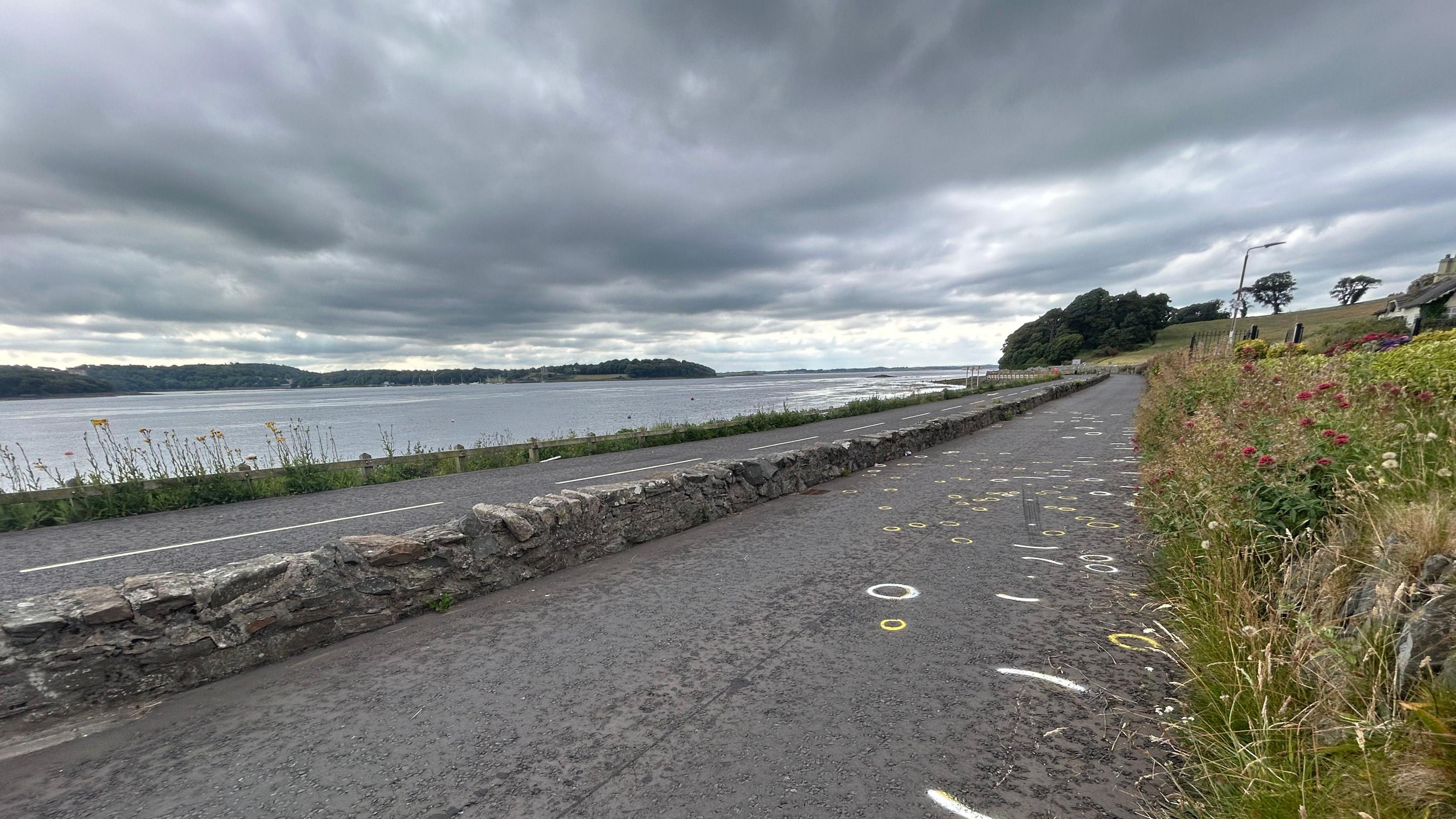 A grey sky, water's edge, and stone road which is The Strand in Portaferry