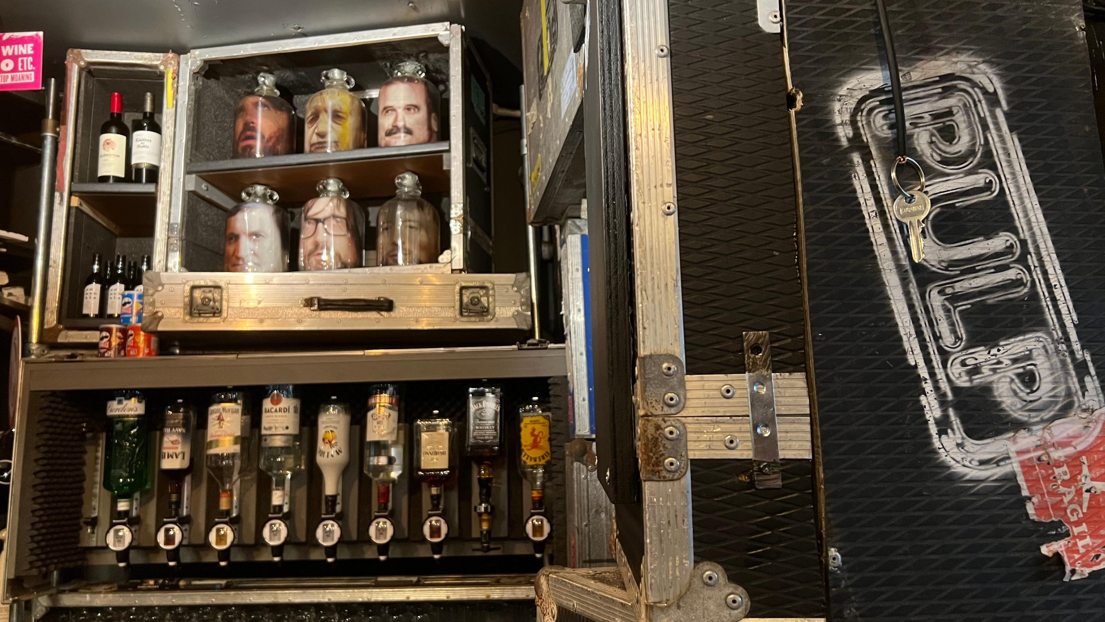 A bar with glass bottle of spirits being held upside down in a flight case. On the right is a flight case with Pulp emblazoned on it