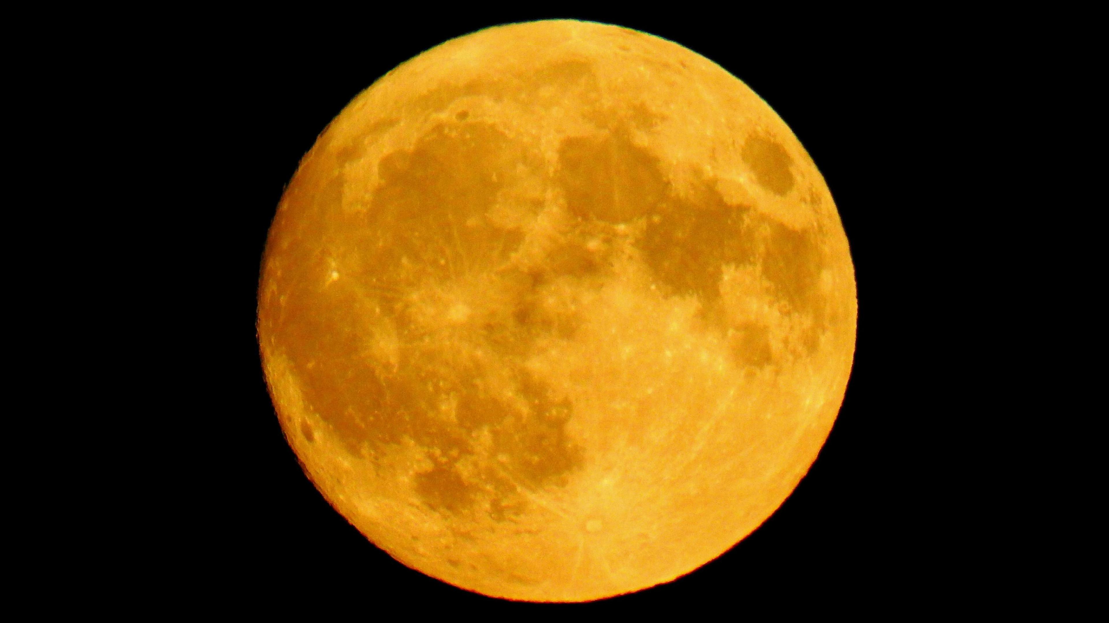 Close-up view of a golden full moon against a black night sky, showing detailed craters and surface markings.