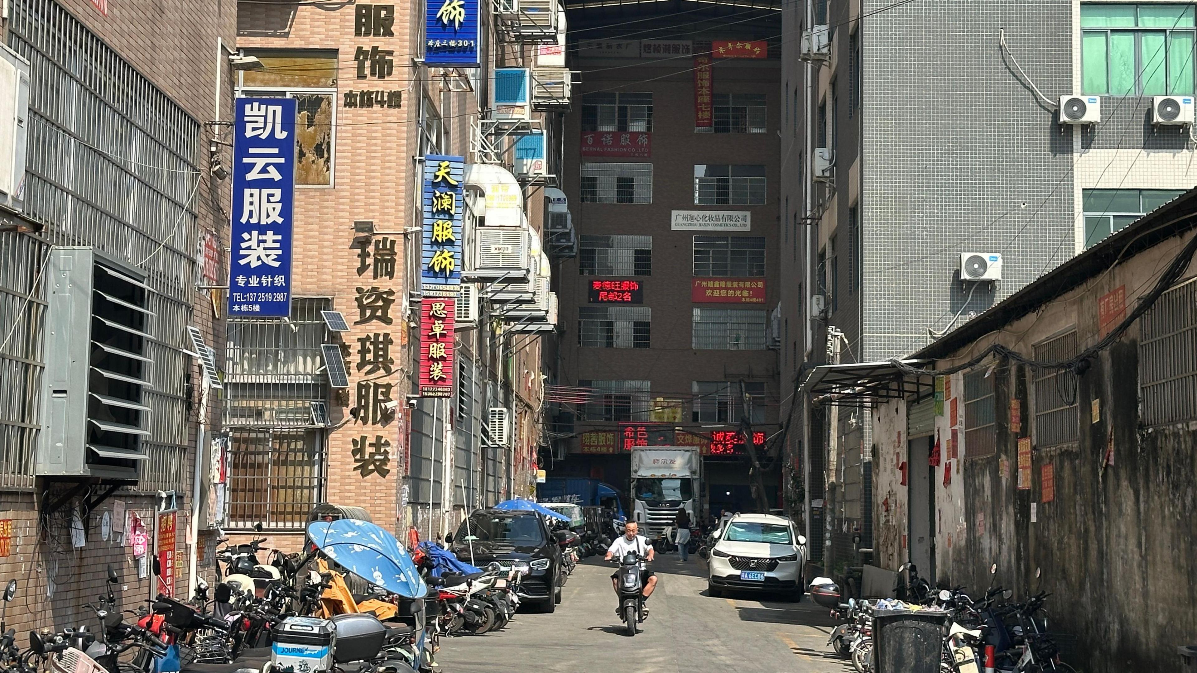 A man on a motorbike drives down a street with buildings on either side 