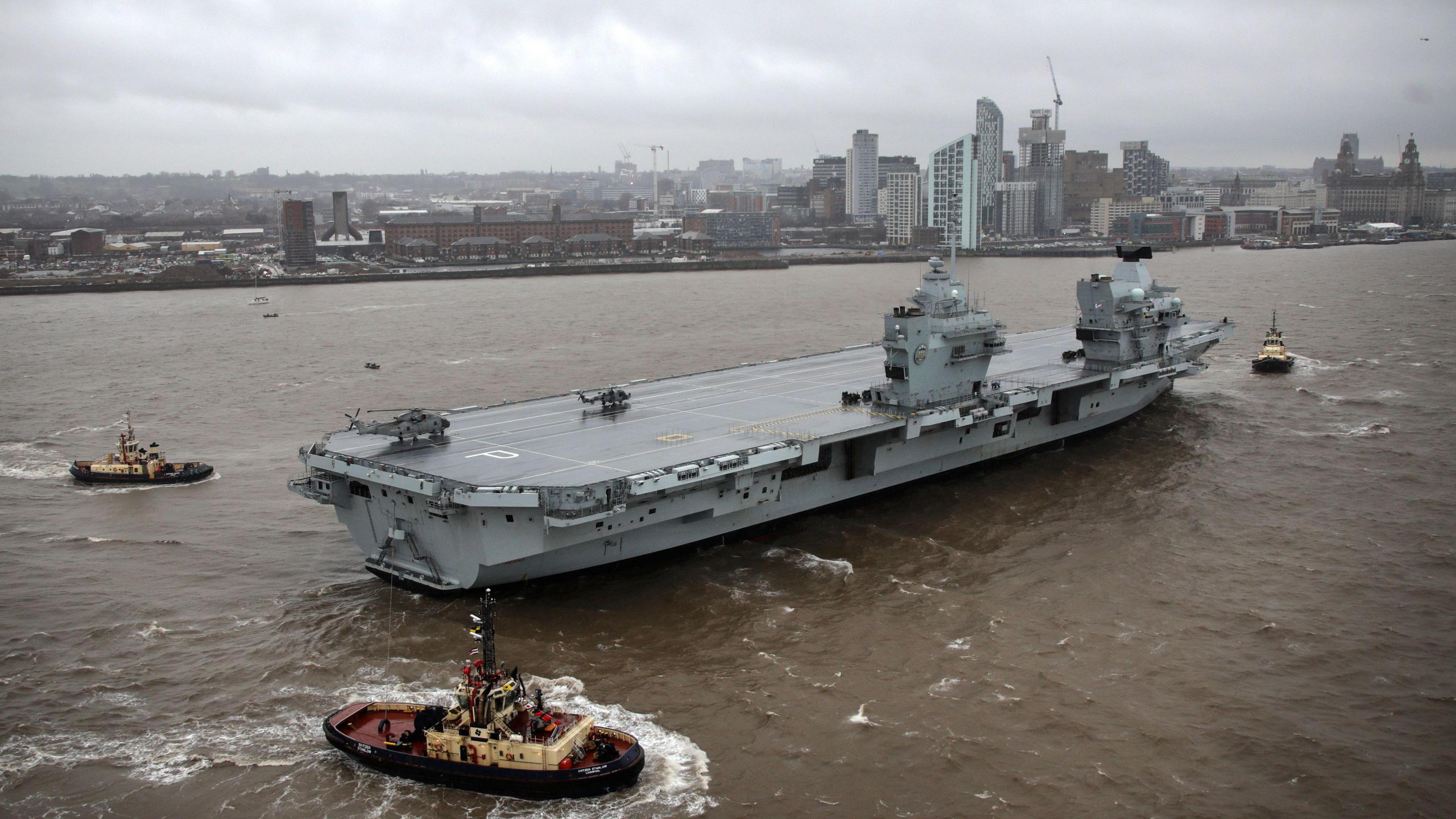 HMS Prince of Wales on the River Mersey, with the Liverpool city skyline in the background showing the tall buildings