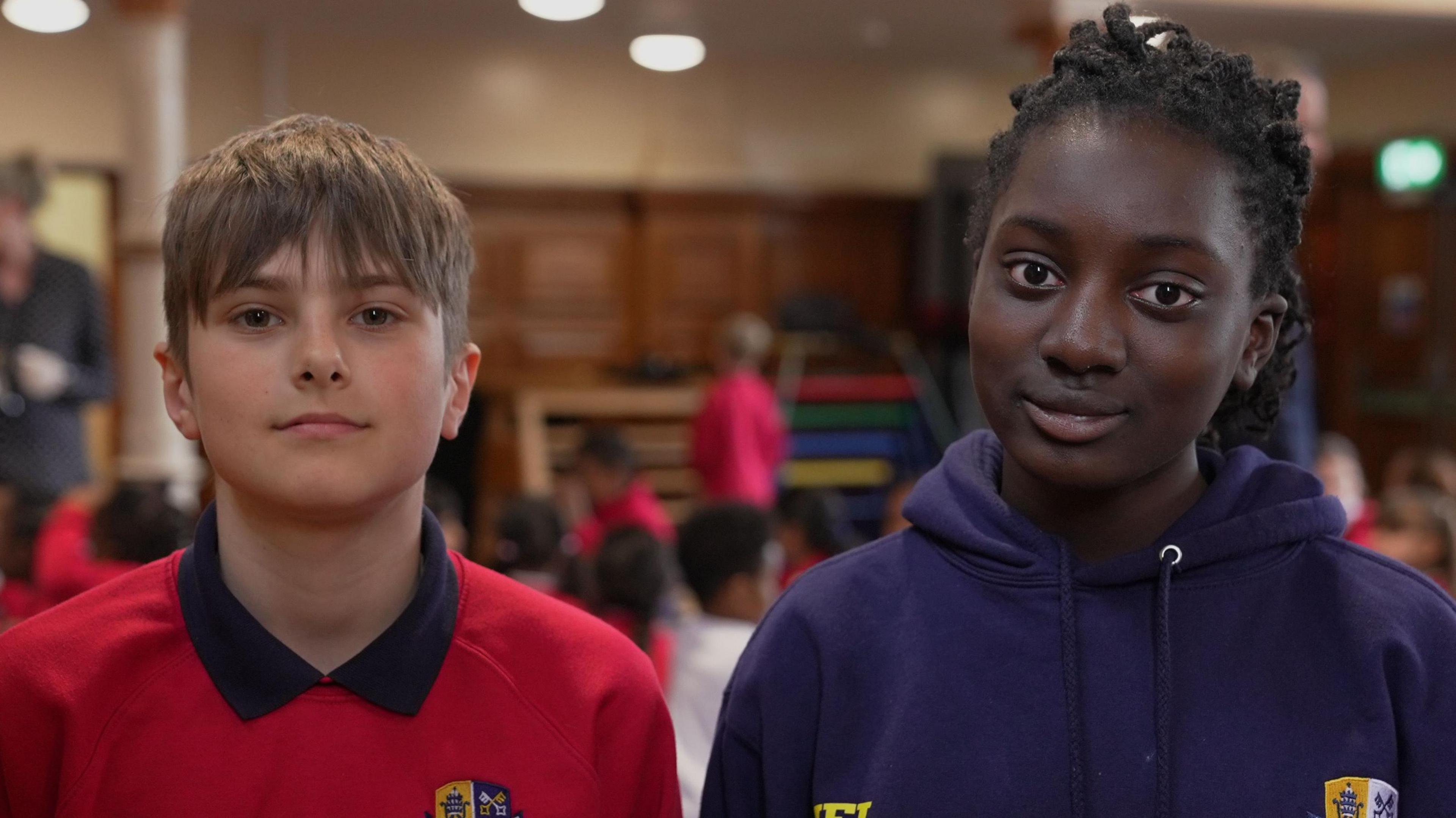 A boy and girl in their school uniforms in front of a hall at dinner time