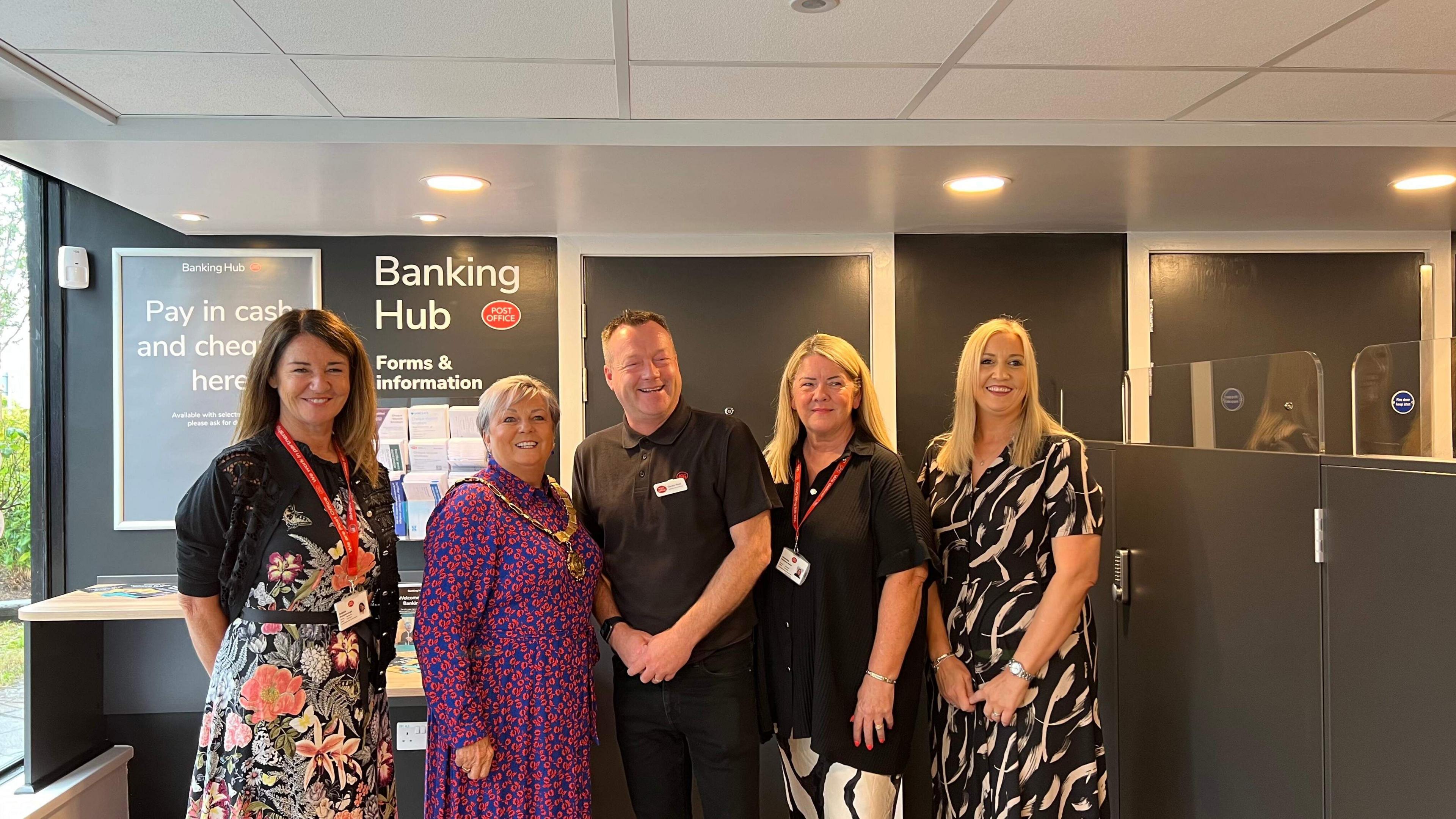 Inside the banking hub which is newly refurbed, Simon stands in the middle of five women including Saltash's mayor who is on his right. All five are facing the camera and smiling.