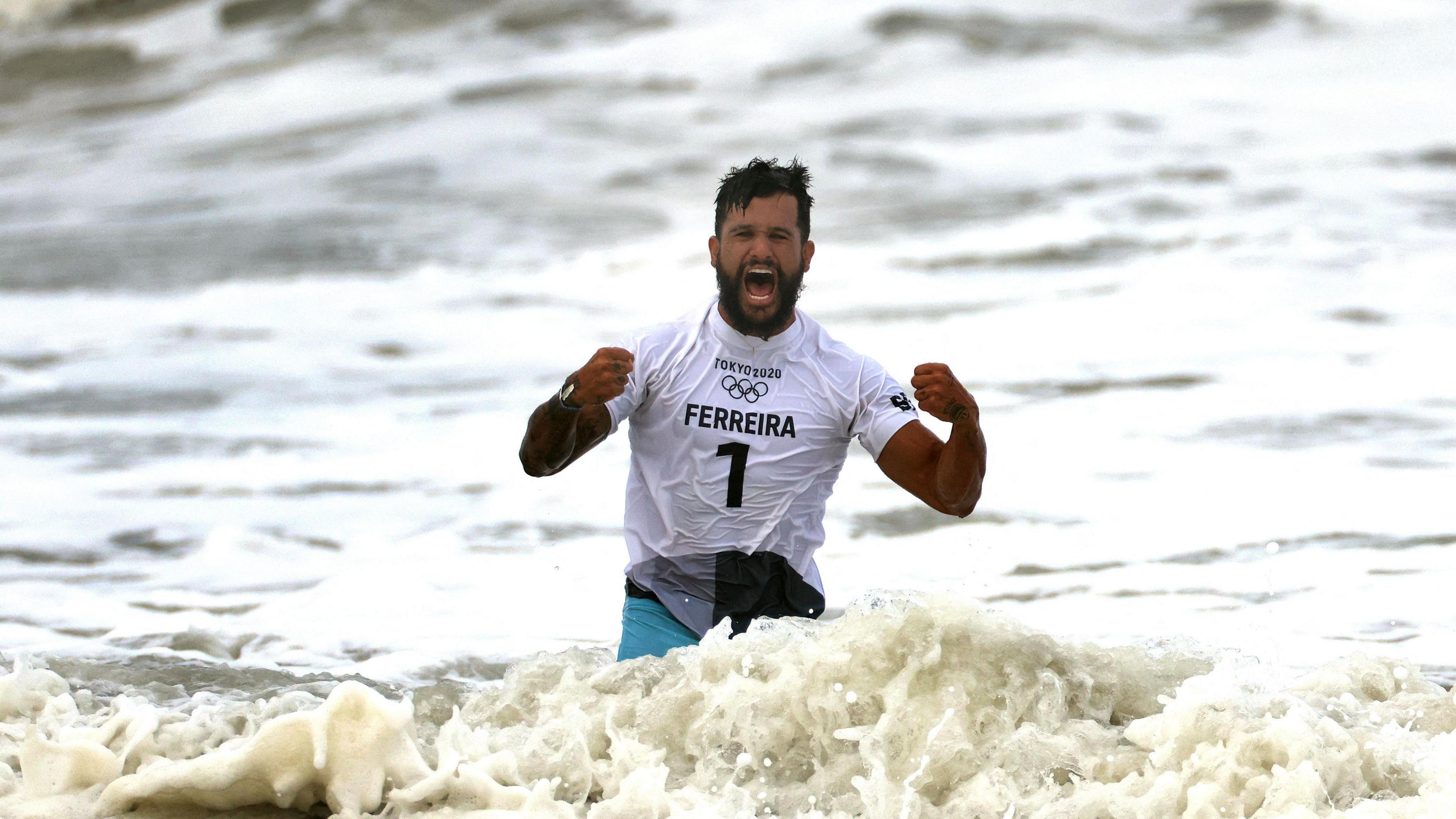 Italo is dressed in a white wet t-shirt emblazoned with his name, number and Olympic logo. He has his hands clenched in fists in celebration 