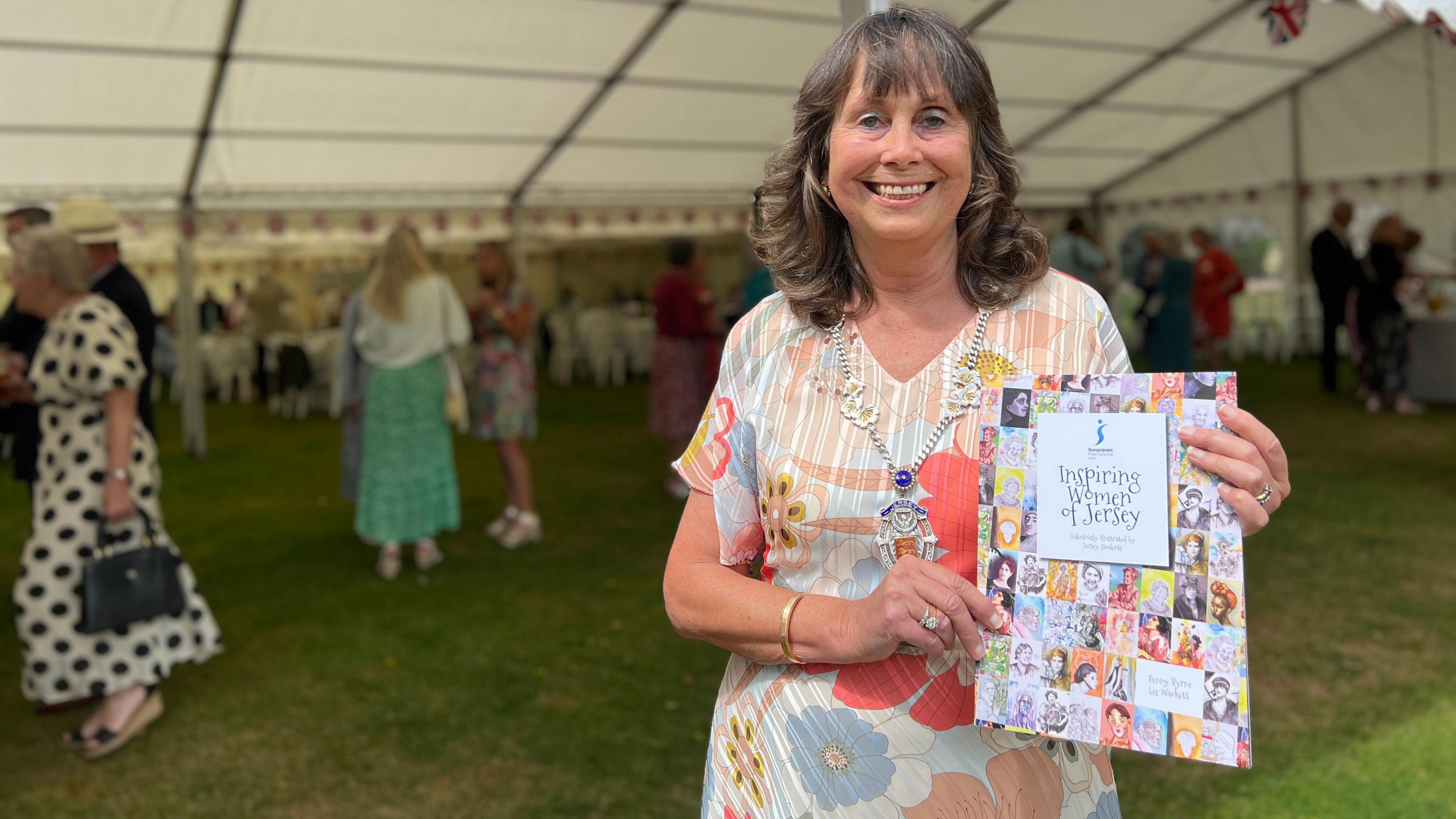 Jean-Marie smiles at the camera as she holds a book about Inspiring Women of Jersey