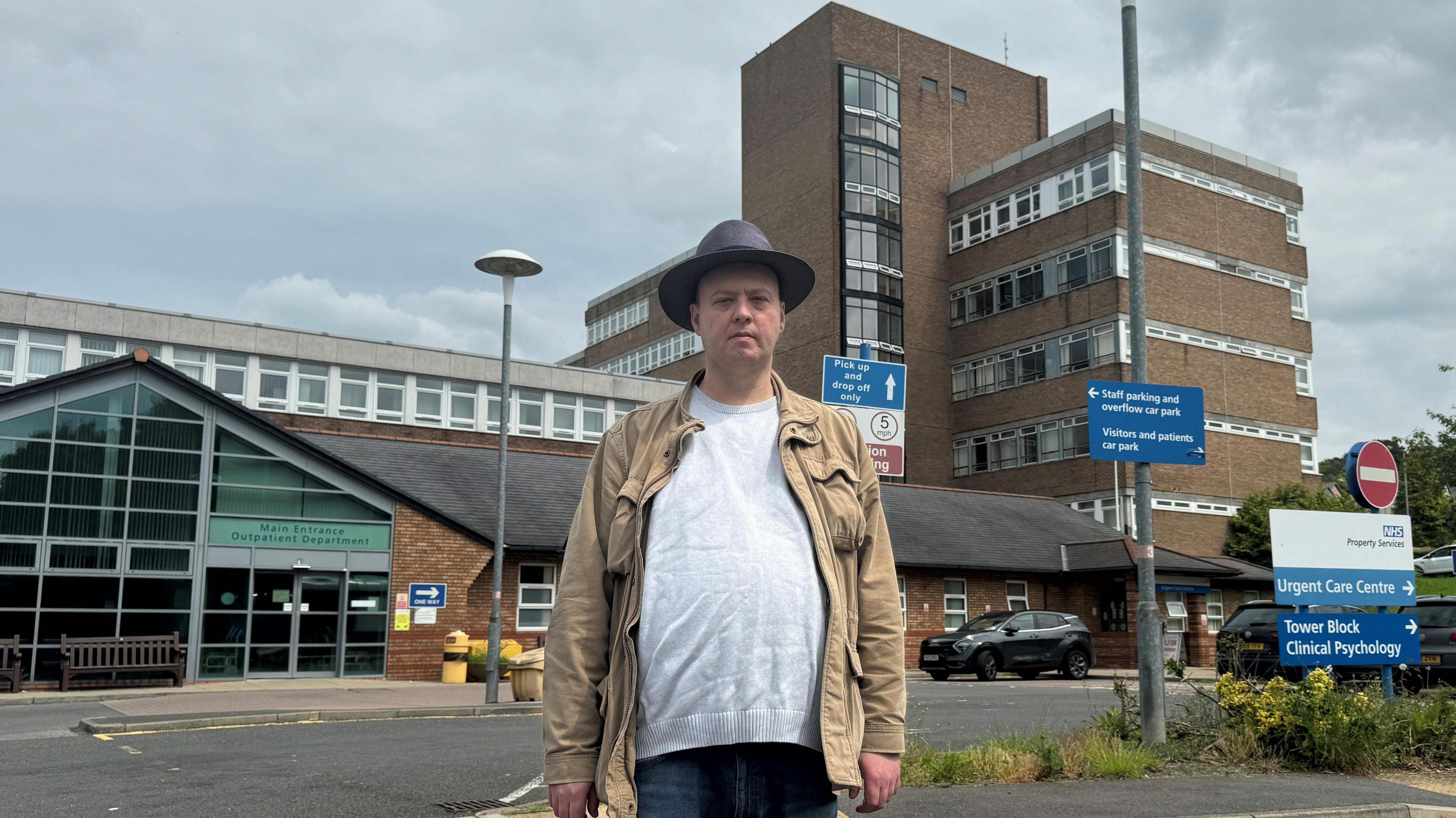 Councillor Dominic Haney standing outside the existing Shotley Bridge Hospital site. He is looking at the camera and he is wearing a light brown jacket, grey top, denim trousers and a dark wide brim hat.