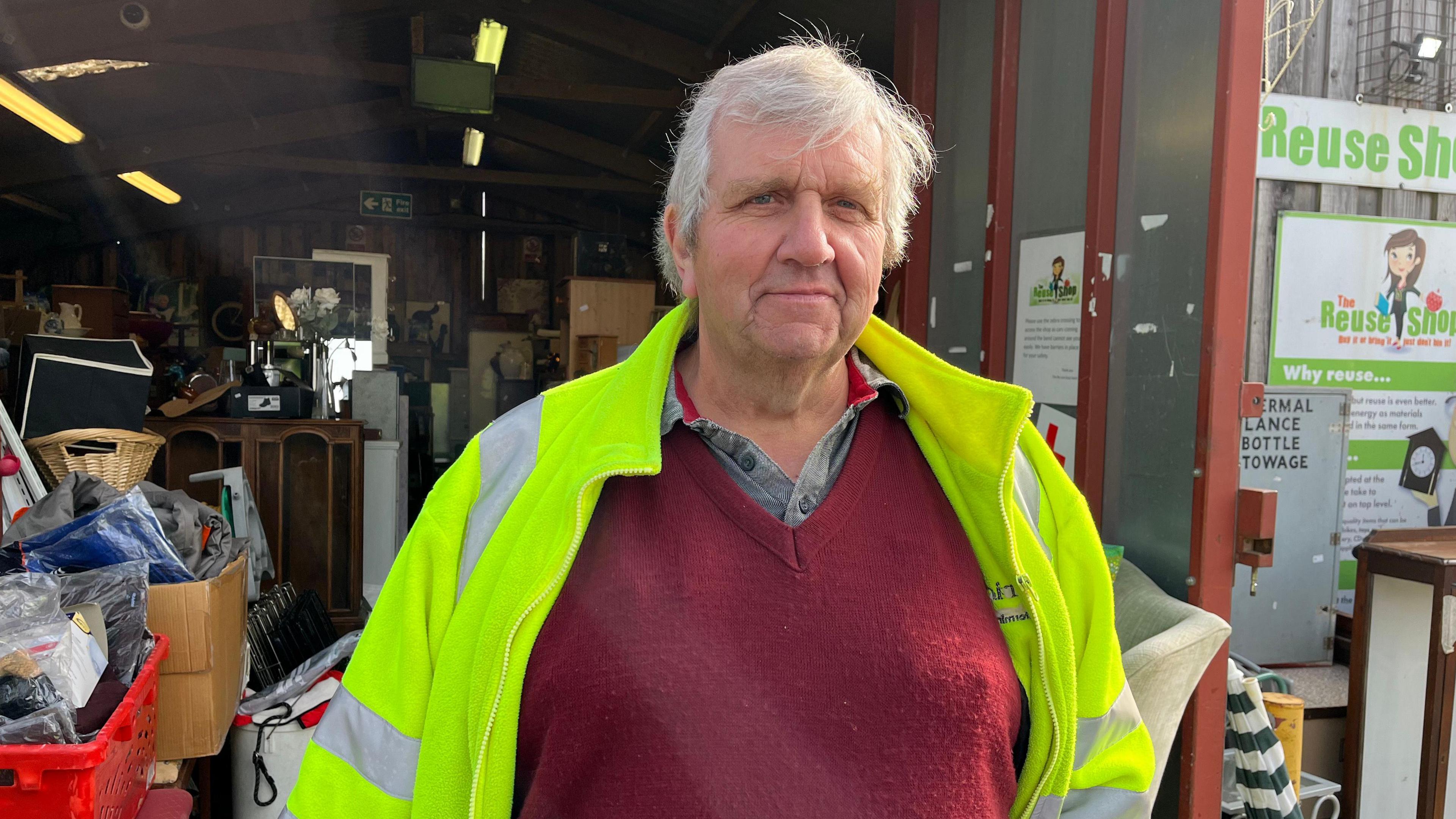 A man wearing a high visibility vest stood infront of the reuse shop doors 