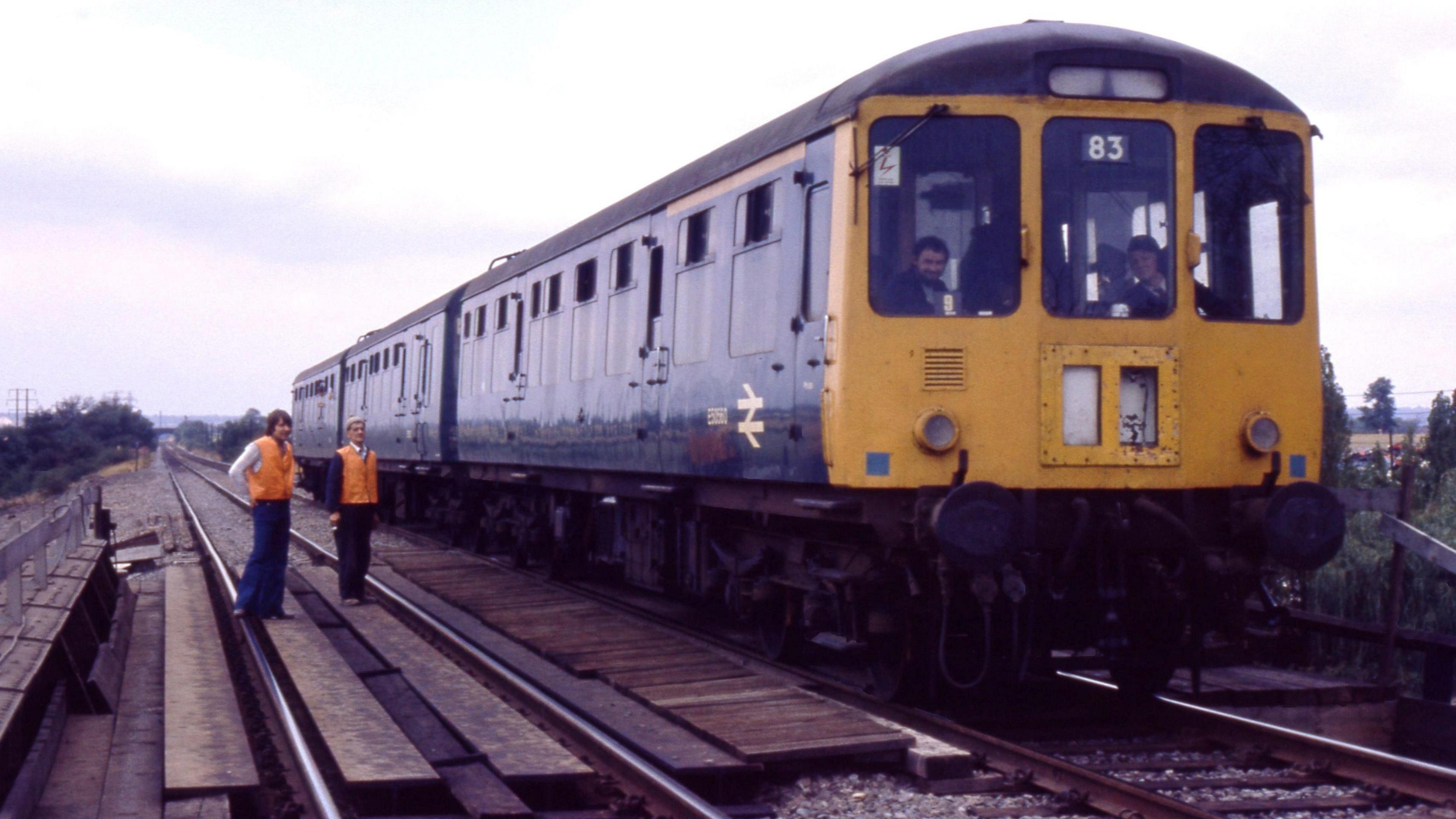 The picture shows a train which has stopped on top of the A5 bridge in Hinckley. Former British Rail engineer Brian Maddison is on the left hand side of the picture, with a colleague. Both are wearing high visibility jackets. They are assessing the scene after repairs to the bridge. 