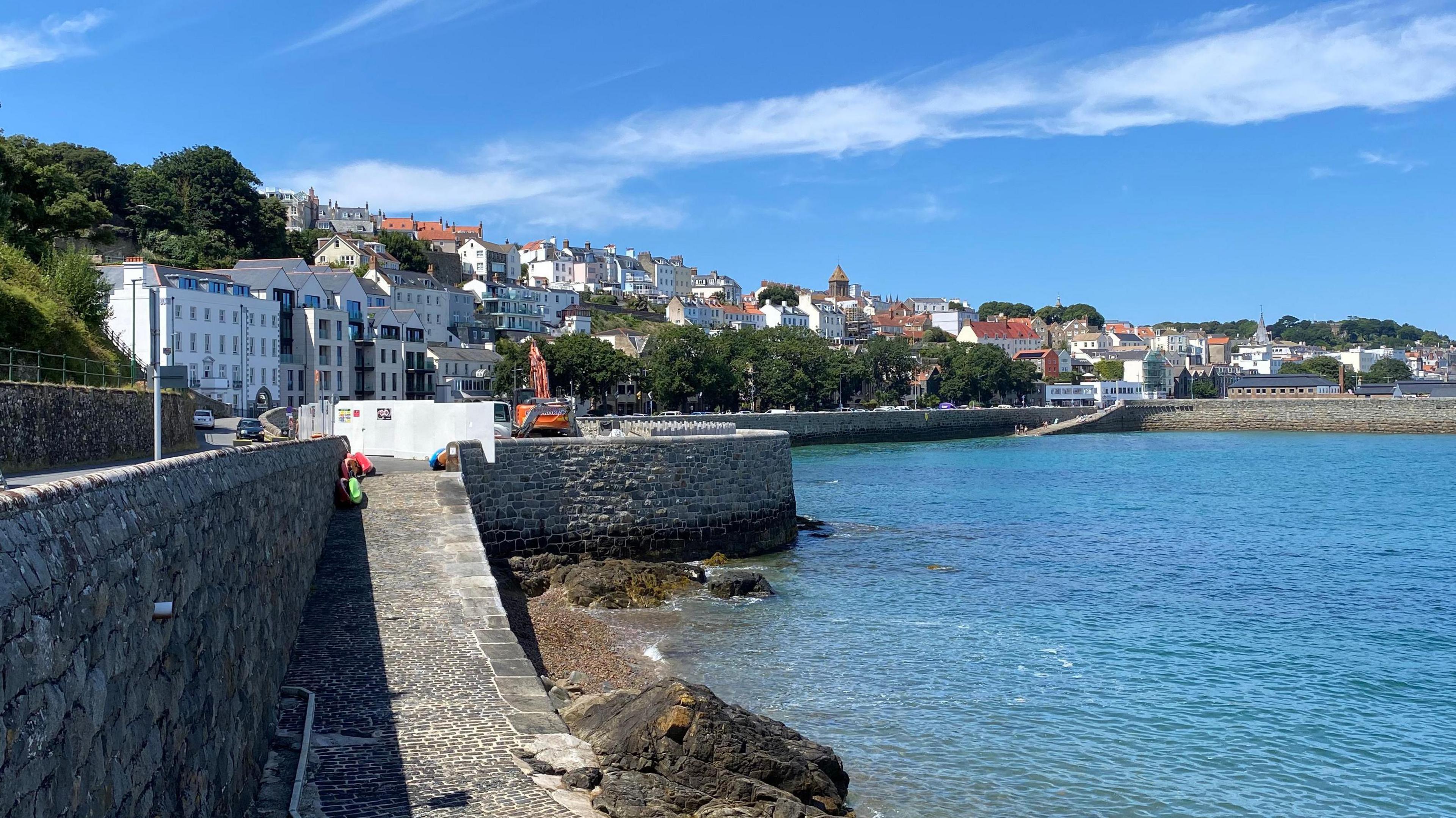 A seafront with a stone slipway and wall and and houses and other buildings behind.