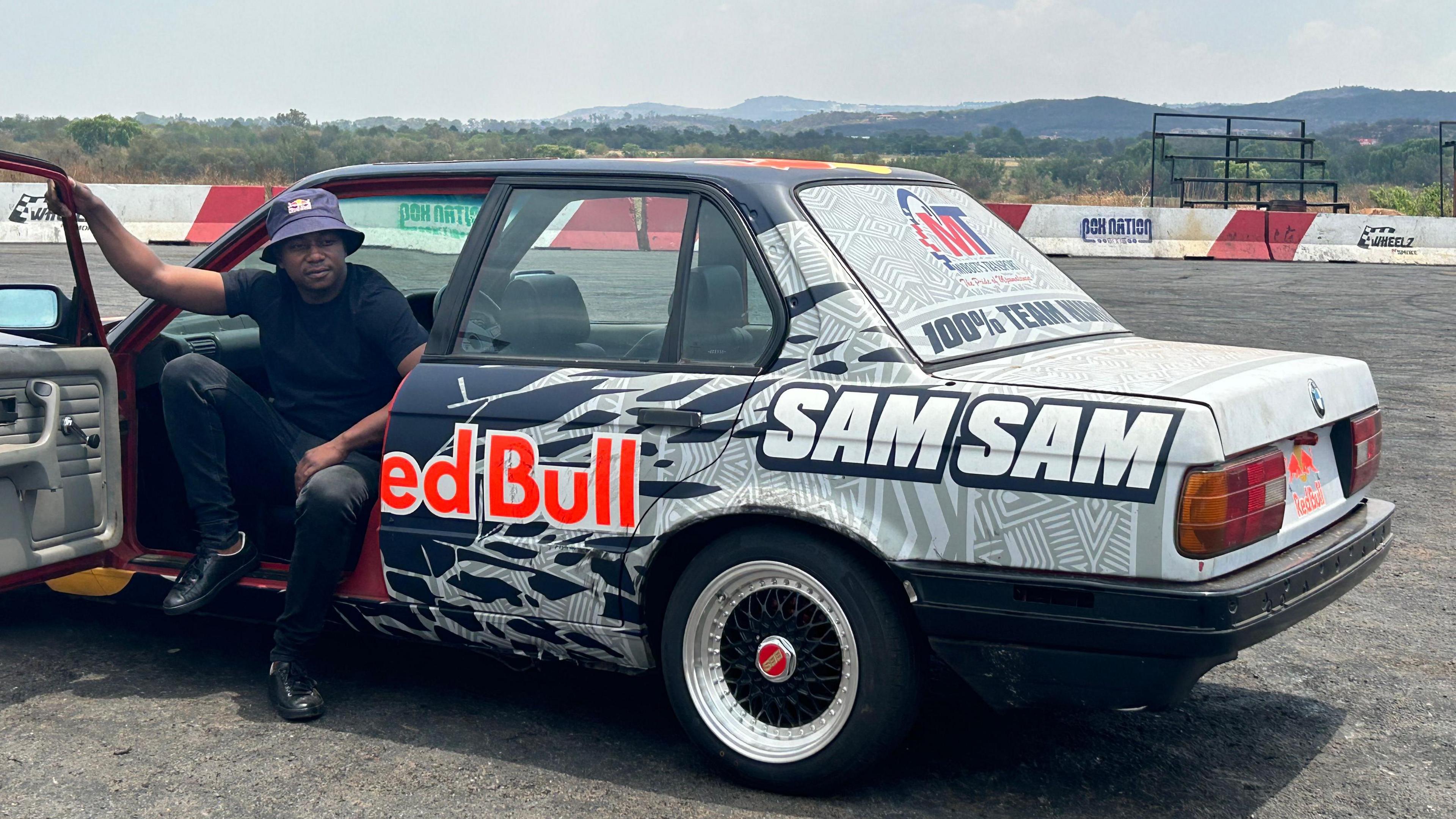 One of South Africa's top spinners Samkeliso Thubane perches on the driver's seat of his grey and dark blue car with his name written on it and with the door open at Wheelz N Smoke, a popular spinning venue in Johannesburg