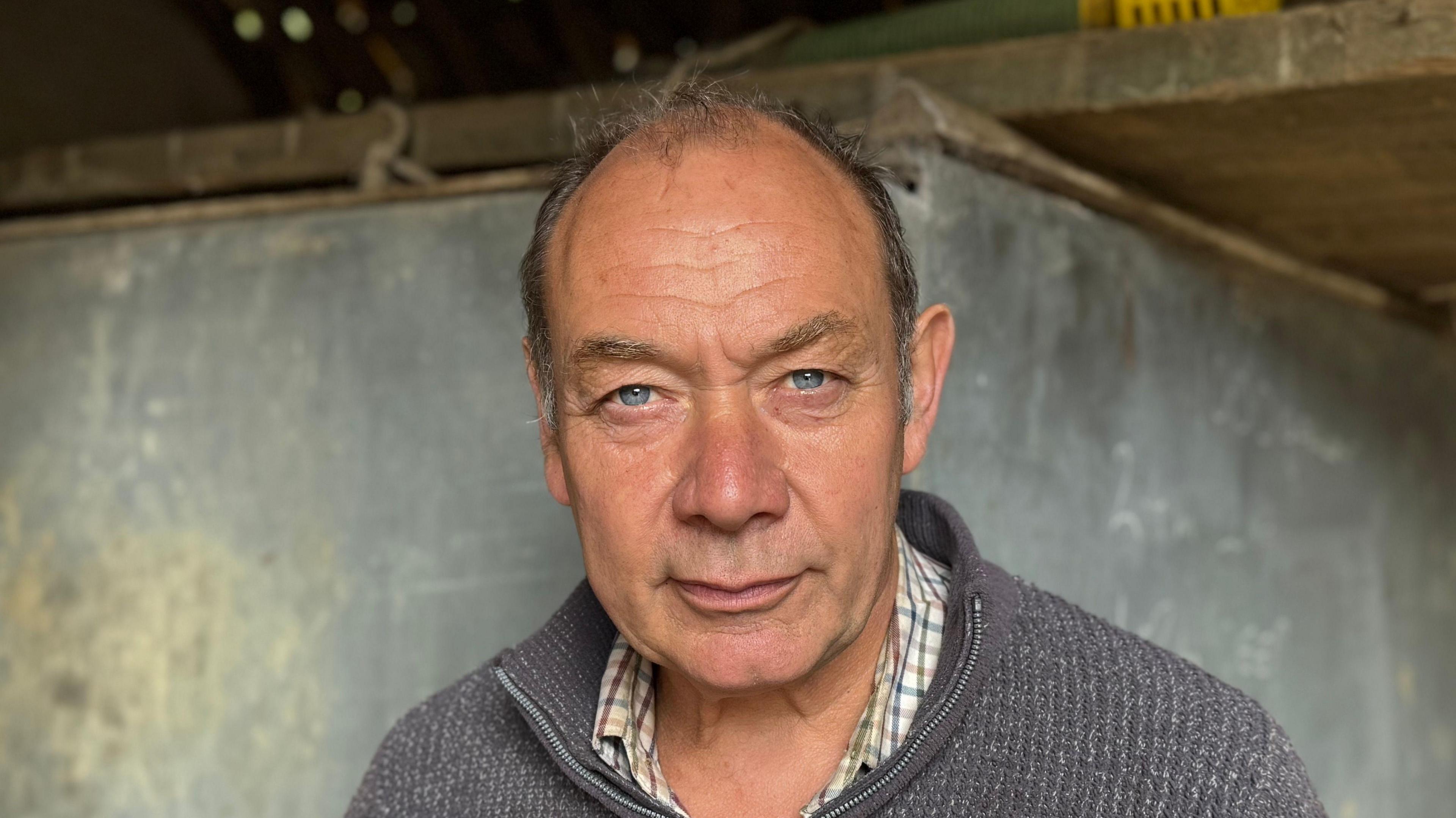 A head and shoulders image of Glenn Buckingham looking directly into the camera. He is wearing a shirt under a piece of knitwear.