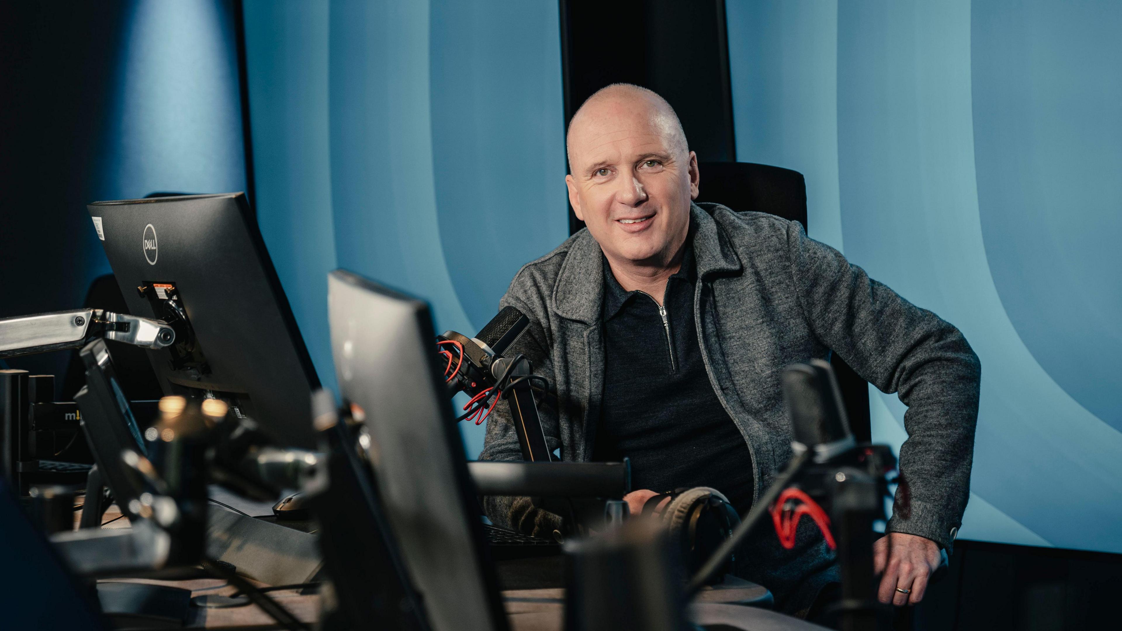 Martin Geissler in the radio studio recording Scotcast. He has a shaved head and is wearing a grey jacket over a black jumper