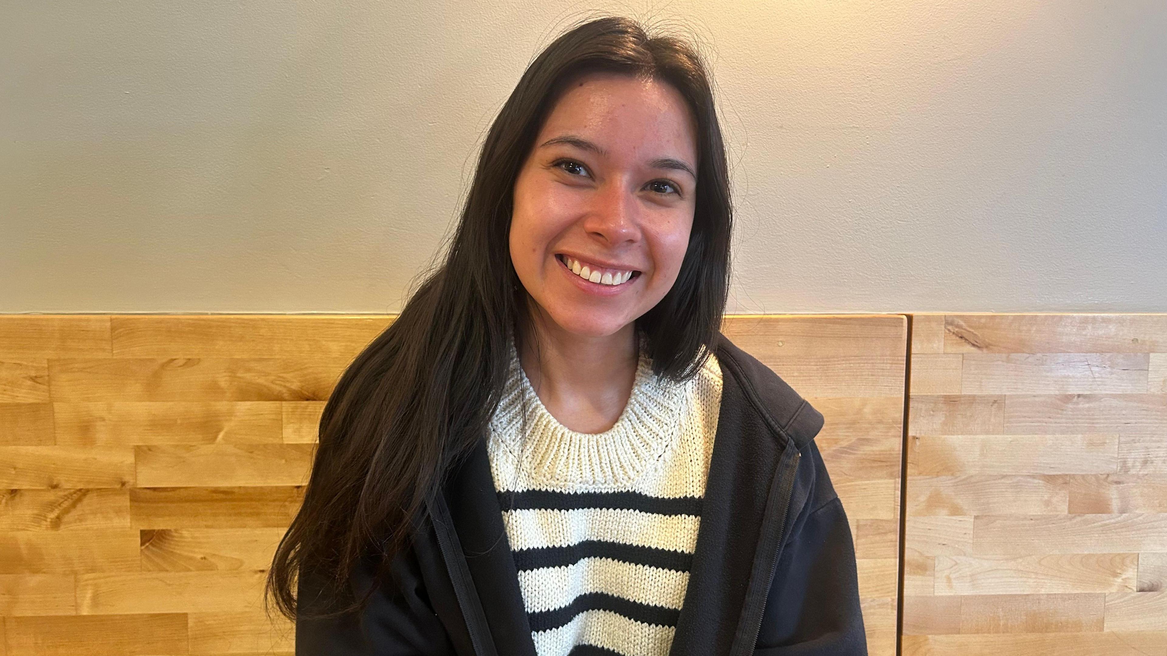 Montana State Representative and Bozeman local Katie Fire Thunder, 25, sits on a bench at a Bozeman coffee shop and smiles, her long dark hair flowing over a white top with black stripes and a black zip-up hoodie