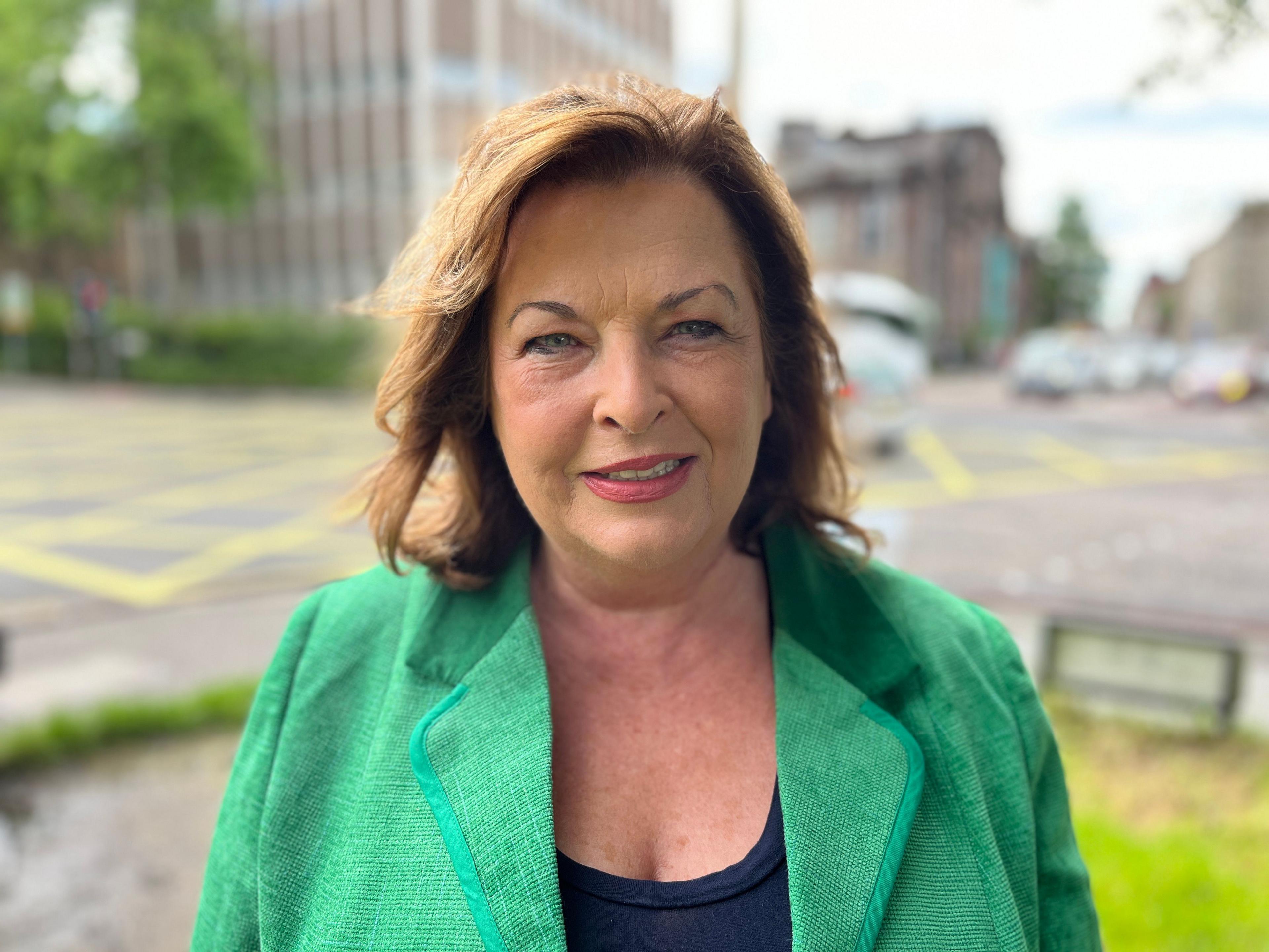 Fiona Hyslop, in a bright green jacket on a busy Edinburgh street