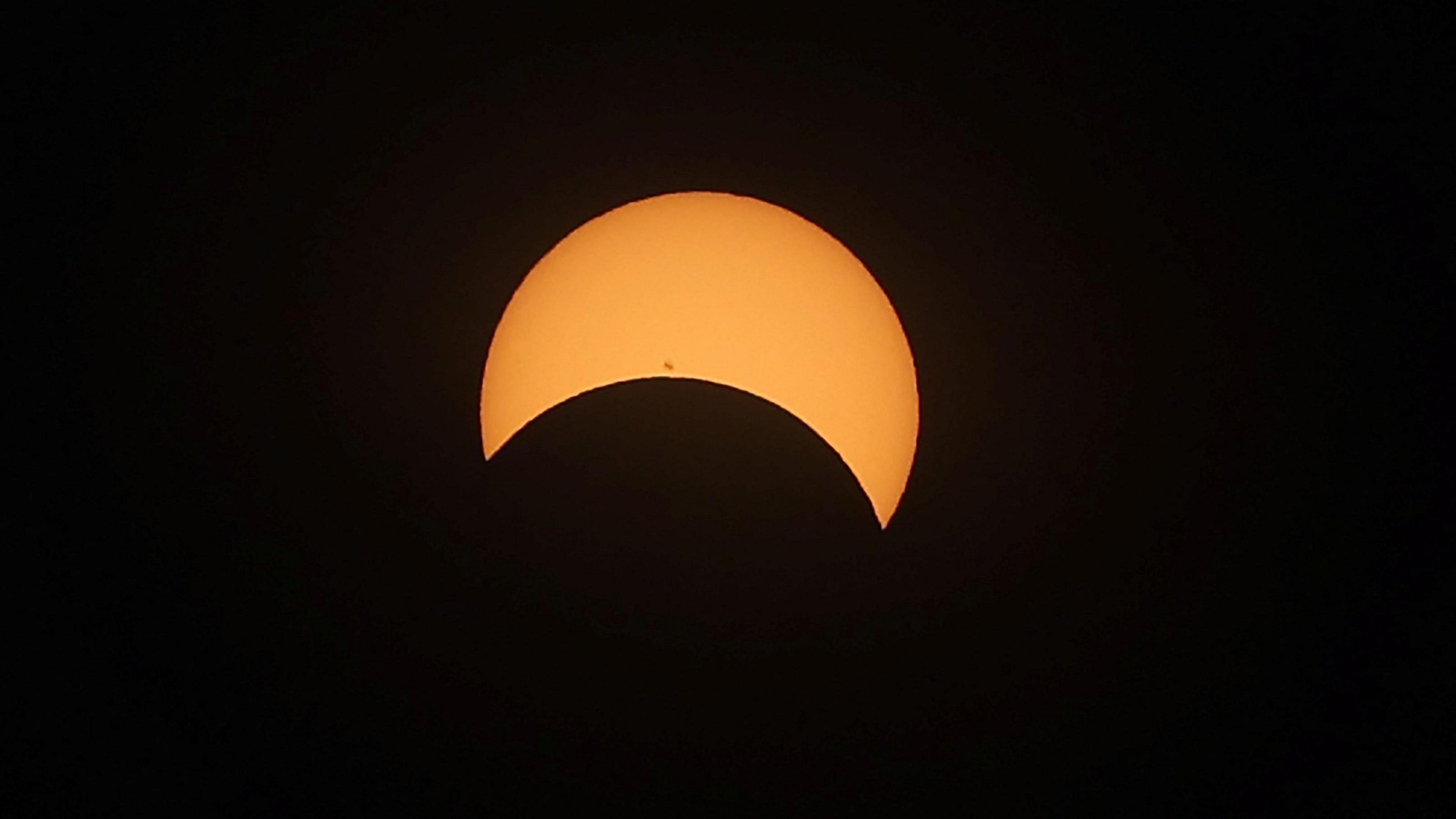 A picture of a partial eclipse showing the bright orange sun with a crescent over its lower half. The background is black.