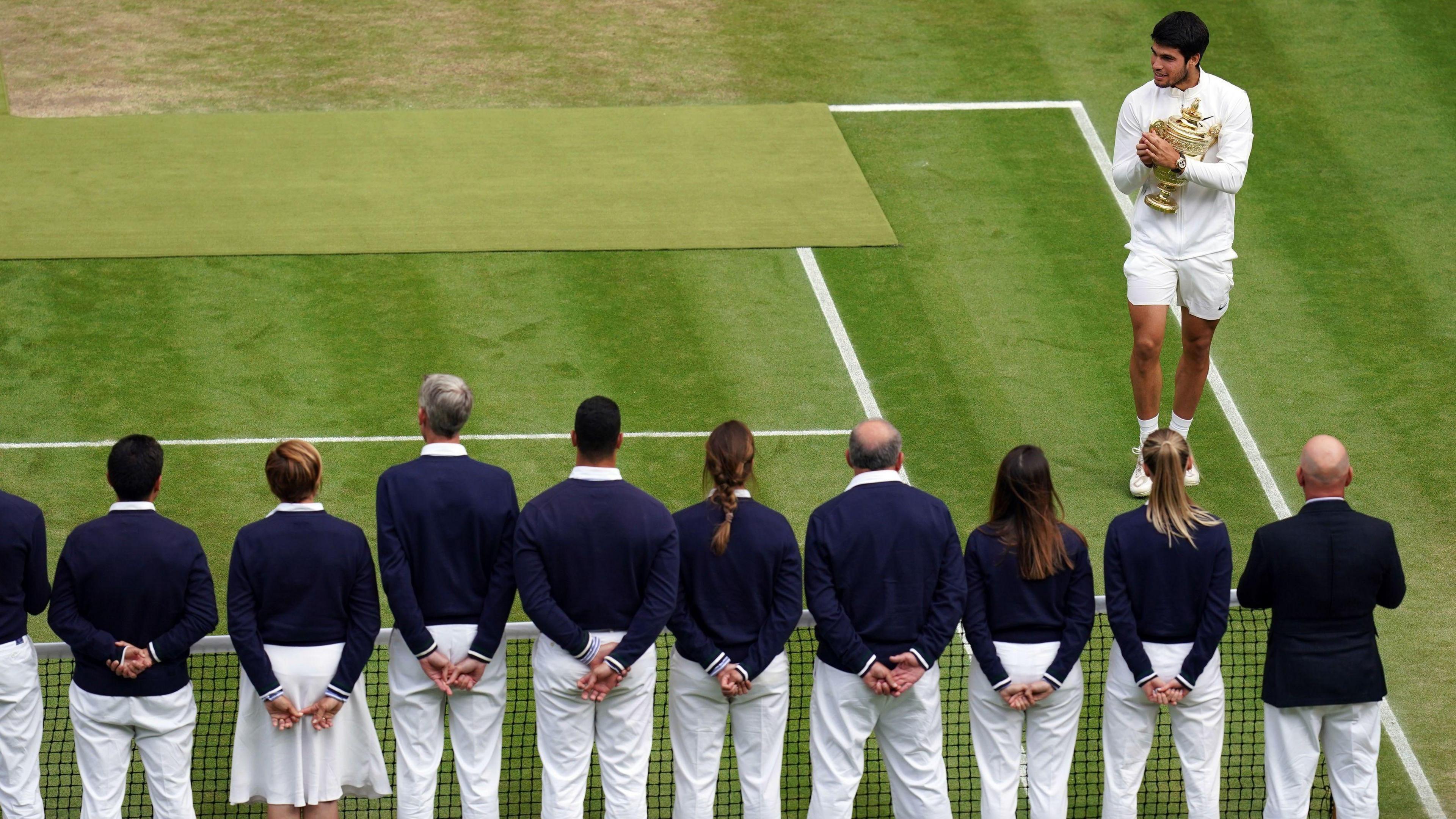 Carlos Alcaraz, the reigning Wimbledon men's singles champion, stands in front of a row of line judges