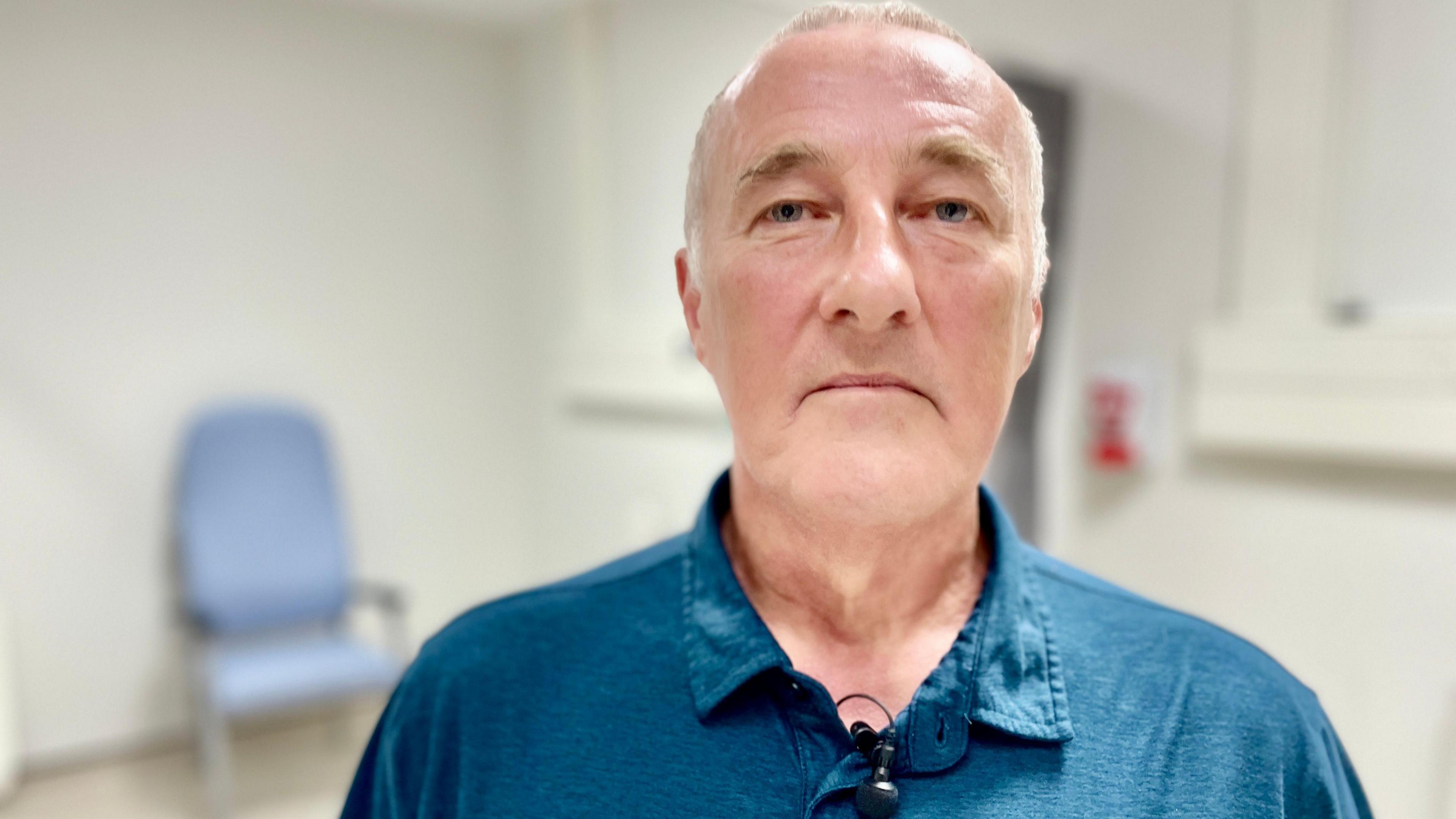 A man with short grey hair wearing a blue shirt standing in a hospital clinic