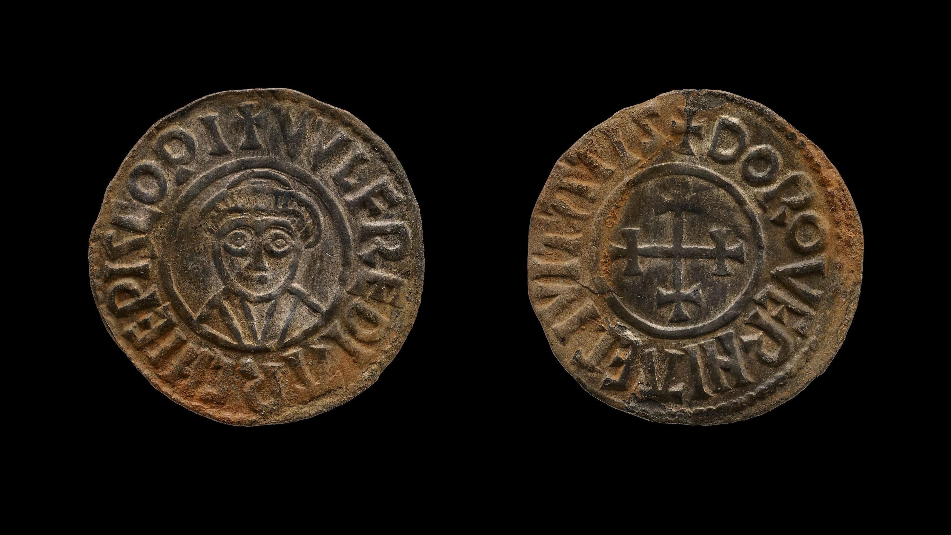 Two sides of a small silver coin.  It dates from the Ninth Century and has been struck using a die.  One side shows a man wearing a hat or crown with large eyes.  The other side shows a cross. Latin is also inscribed on both sides of the coin.