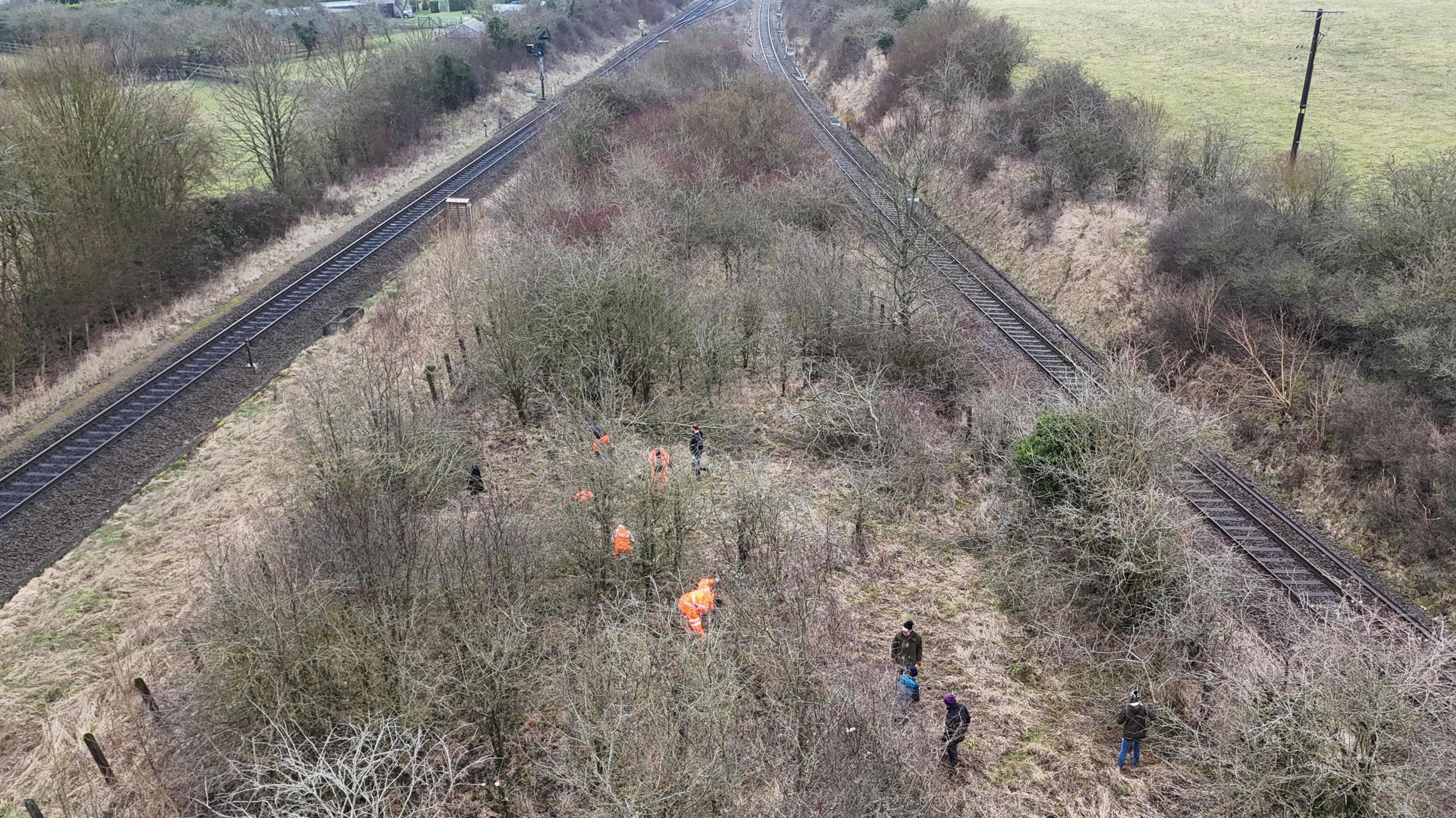 A number of volunteers working between two railway tracks, the photo is taken from above, and shows about nine people, working from a distance. 