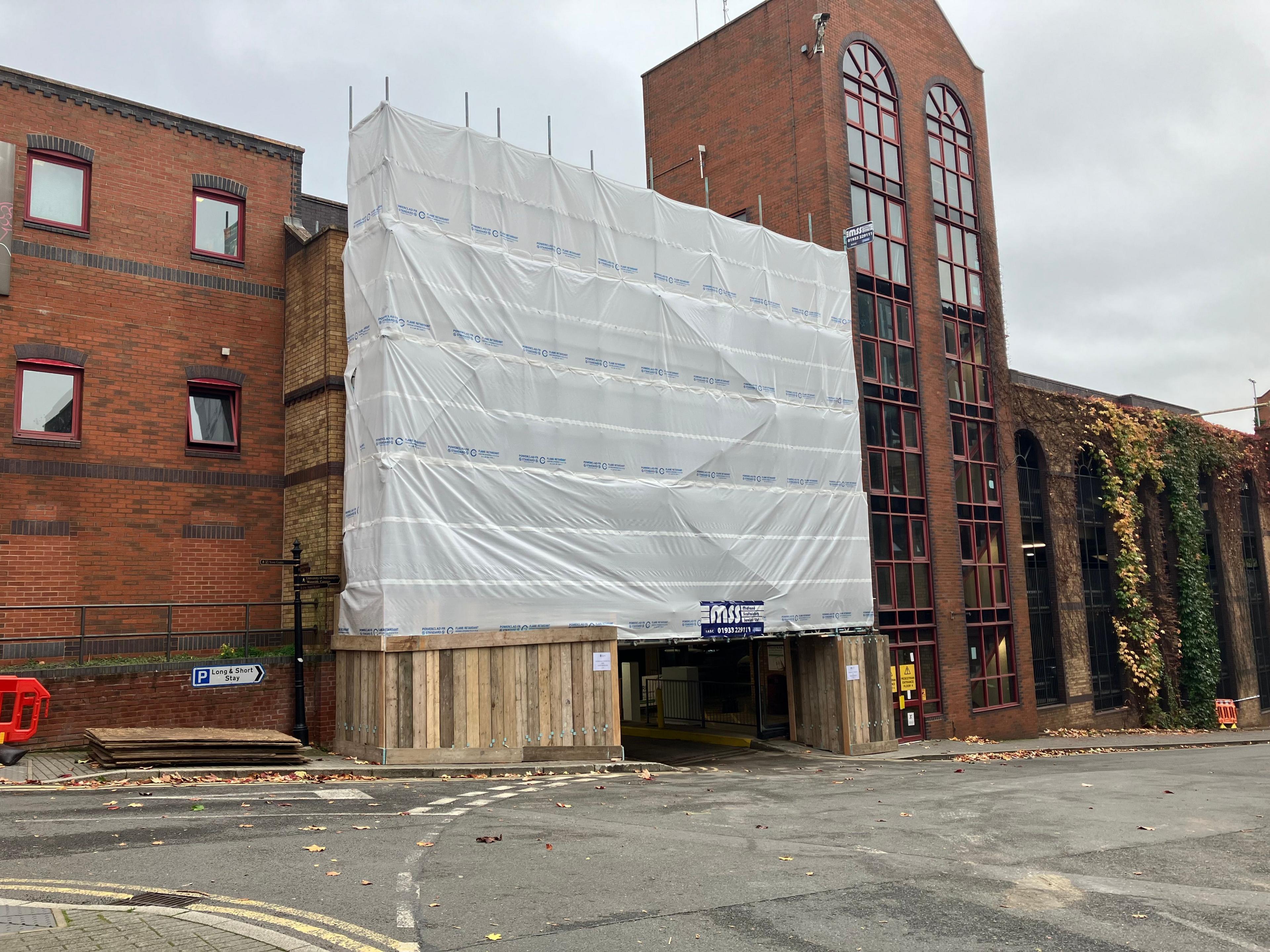 St John's multi-storey car park in Northampton. There is a huge, protective white plastic sheet covering the car park. There is scaffolding behind it.