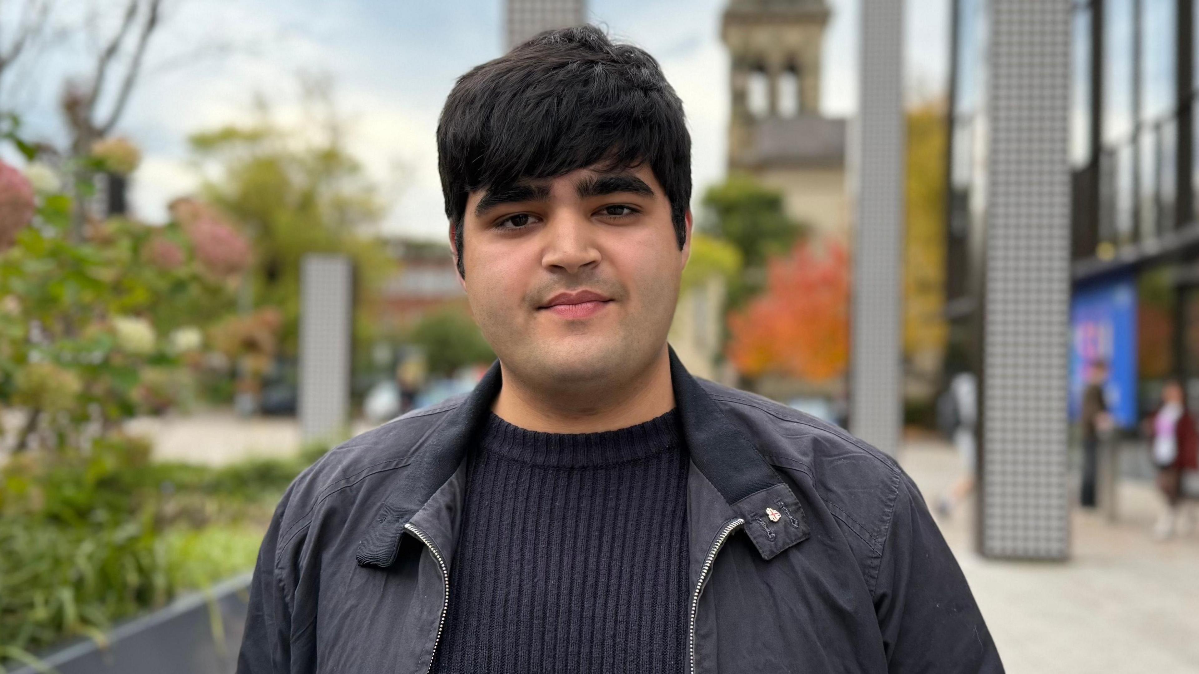 Queens University student Jay Basra standing in front of the university's students' union - he is wearing a dark jacket and navy jumper.