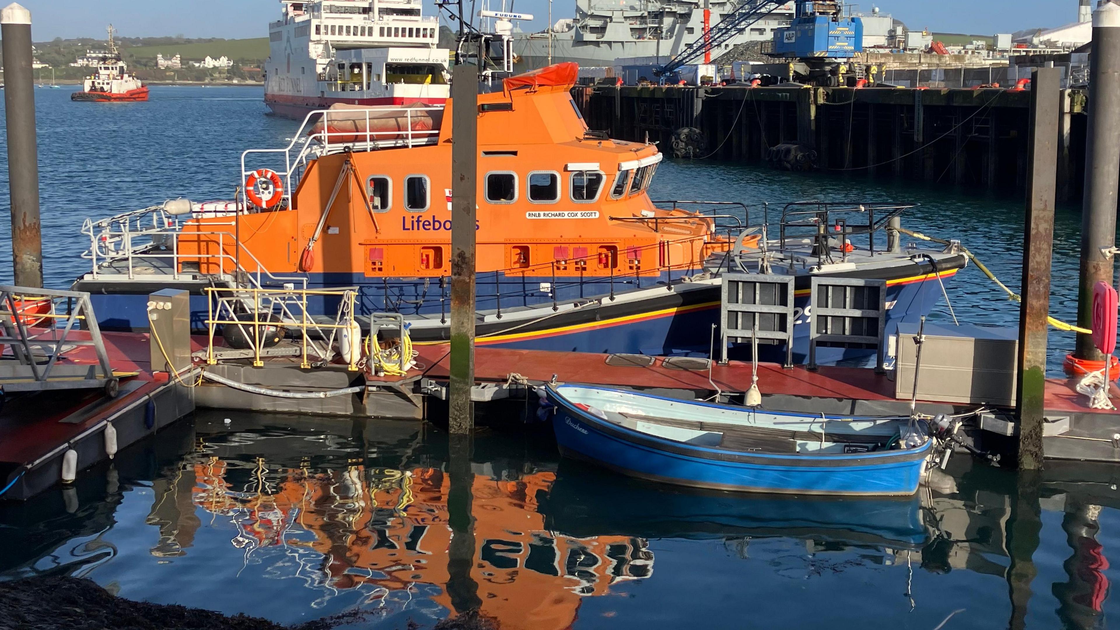 The image of the orange Richard Cox Scott is reflected in the sea in front of her.