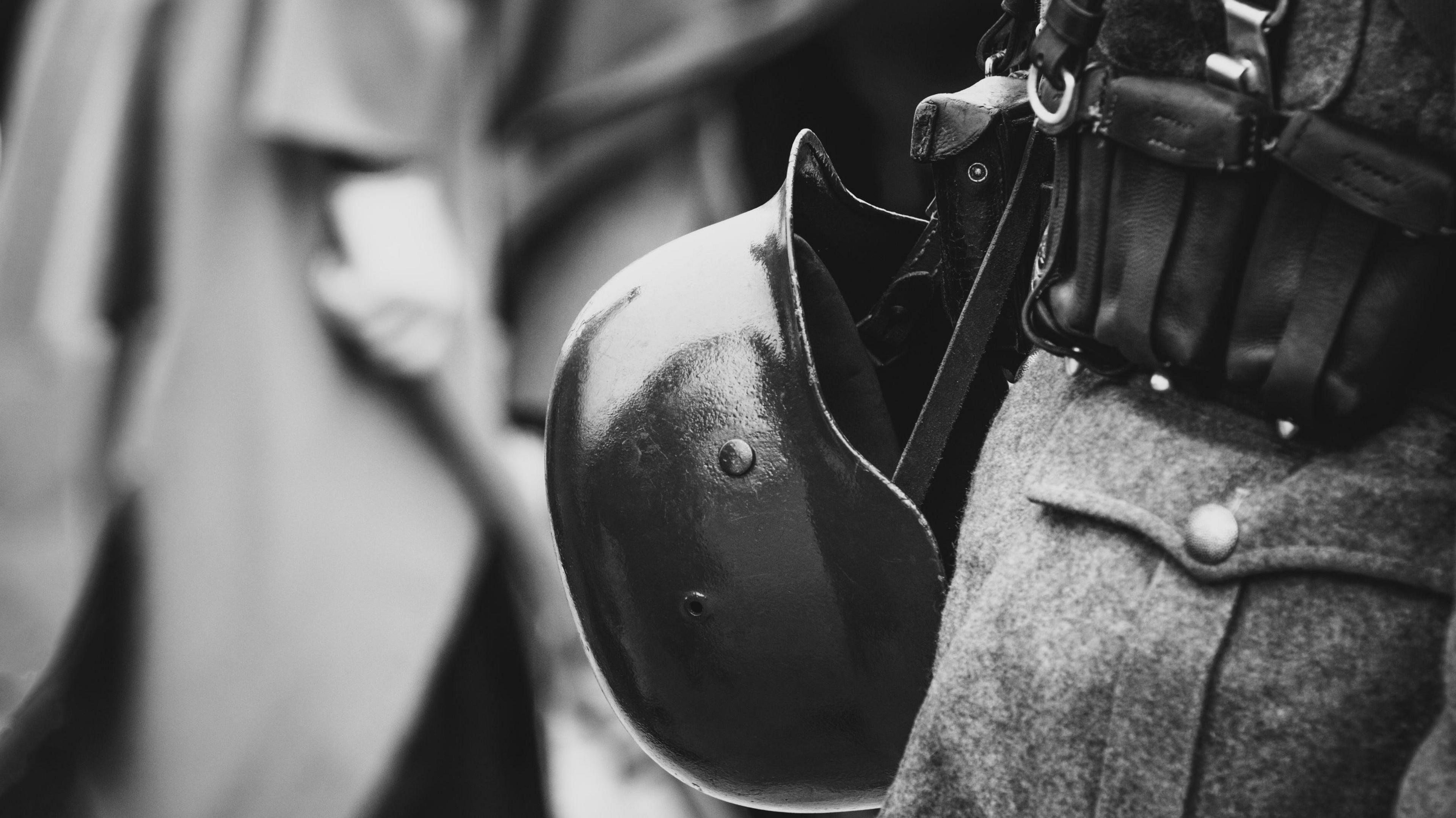 Generic black and white image of a the back of a soldiers belt with helmet attached.