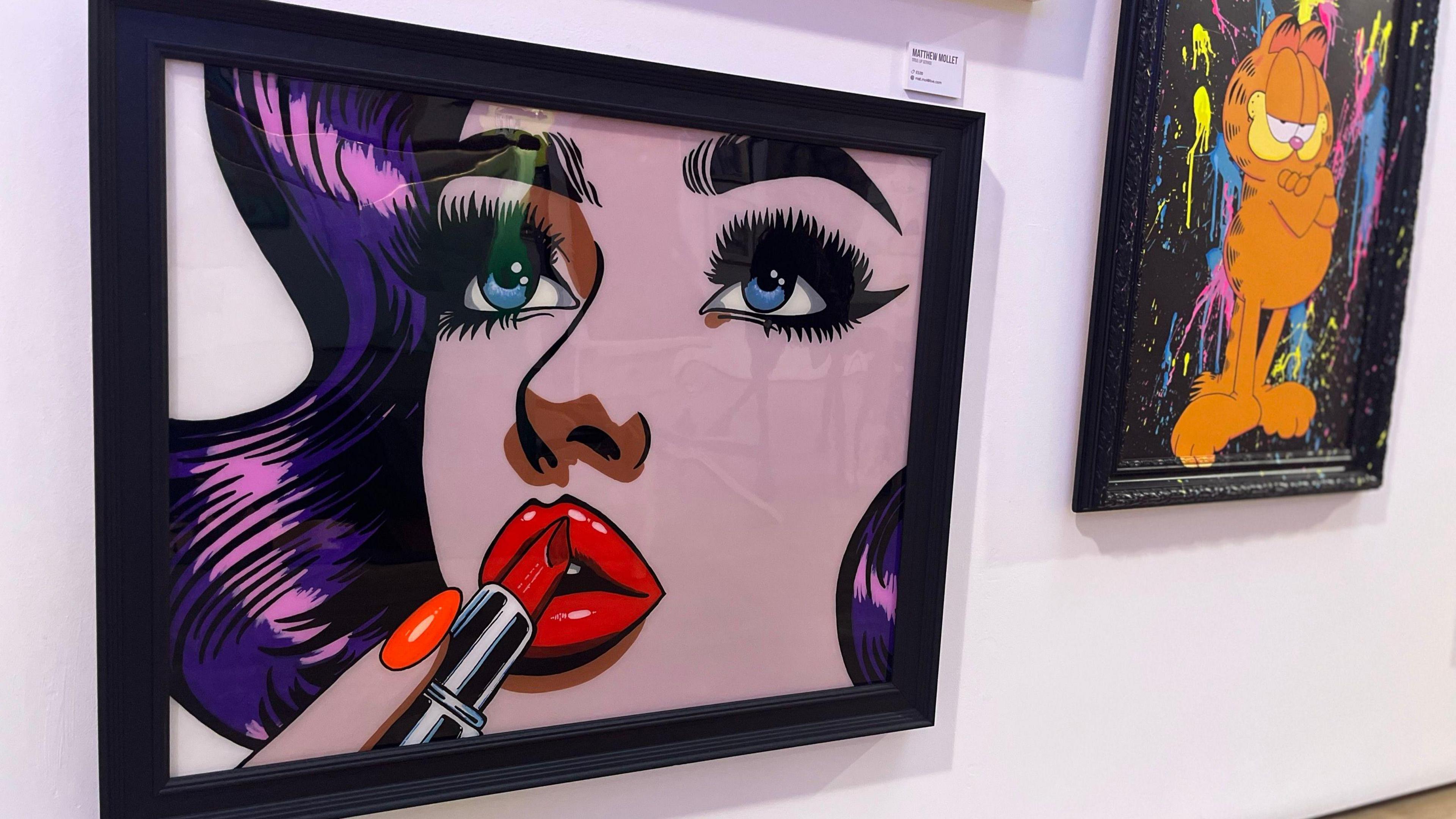 A pop art picture of a woman putting on make up next to a bright painting of the cartoon character Garfield.