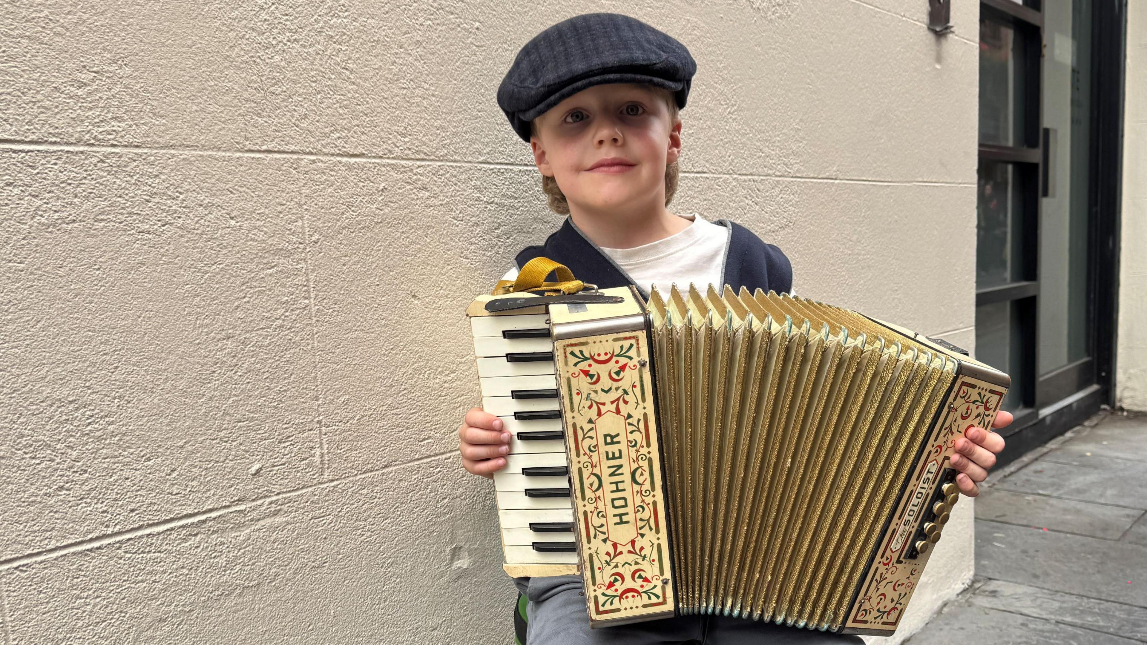 A child with blonde hair wearing a hat and holding an accordian