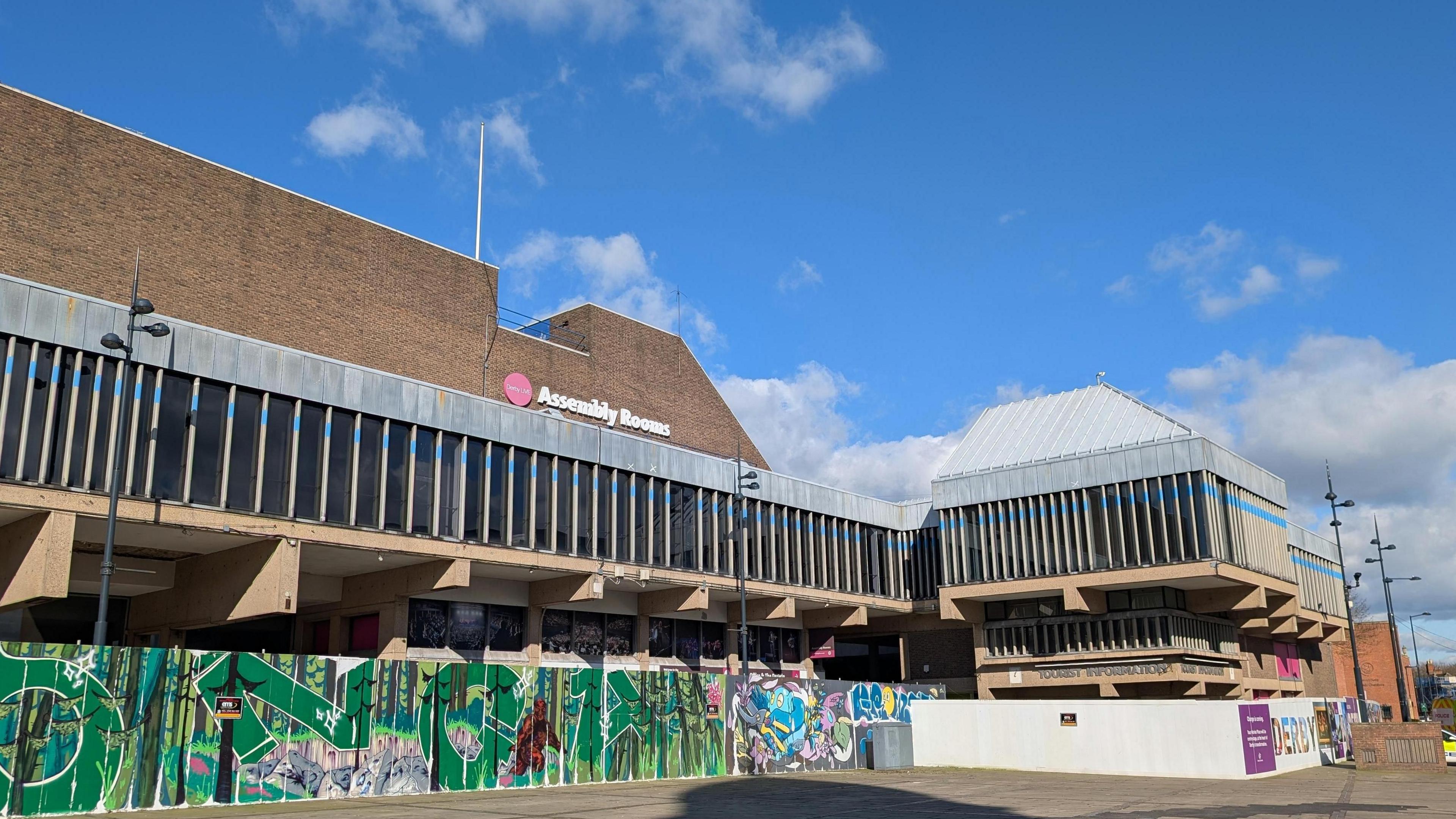 Grey rectangular building with graffiti wall infront and large grey rectangular windows 